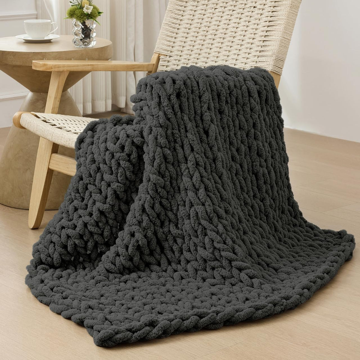Charcoal chunky knit throw draped over a woven chair and cascading to the floor
