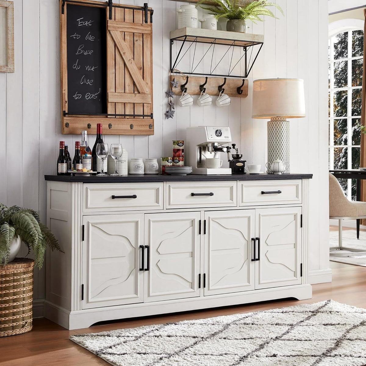 Staged off white sideboard used as a coffee bar with espresso machine, bottles, and lamp on the dark tabletop