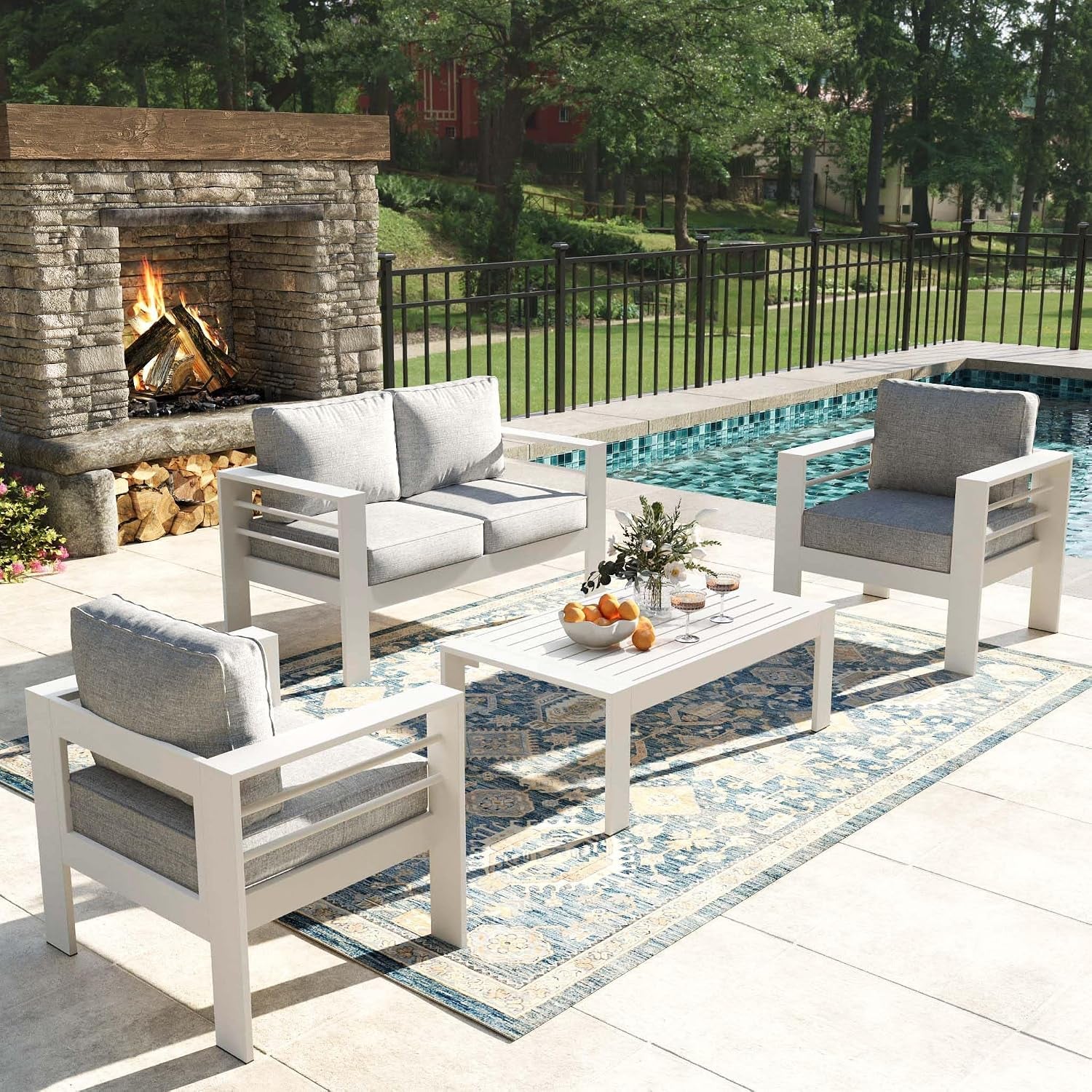 Side perspective of the white aluminum patio set on a tiled deck with a lit stone fireplace.