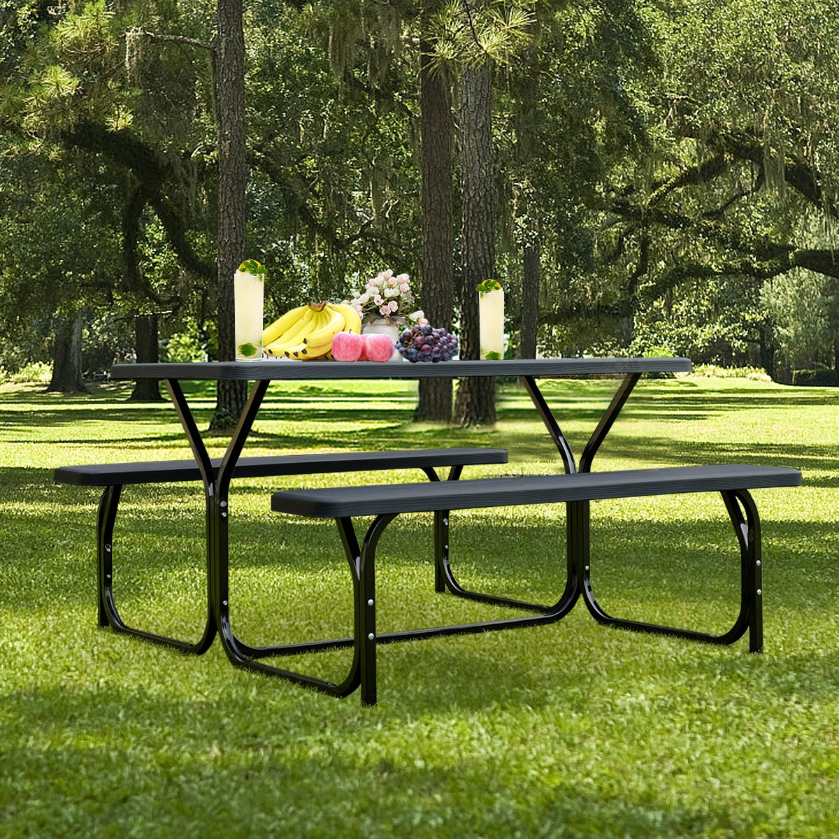 Dark picnic table and two benches on a lawn, with fruit and drinks arranged on the tabletop.