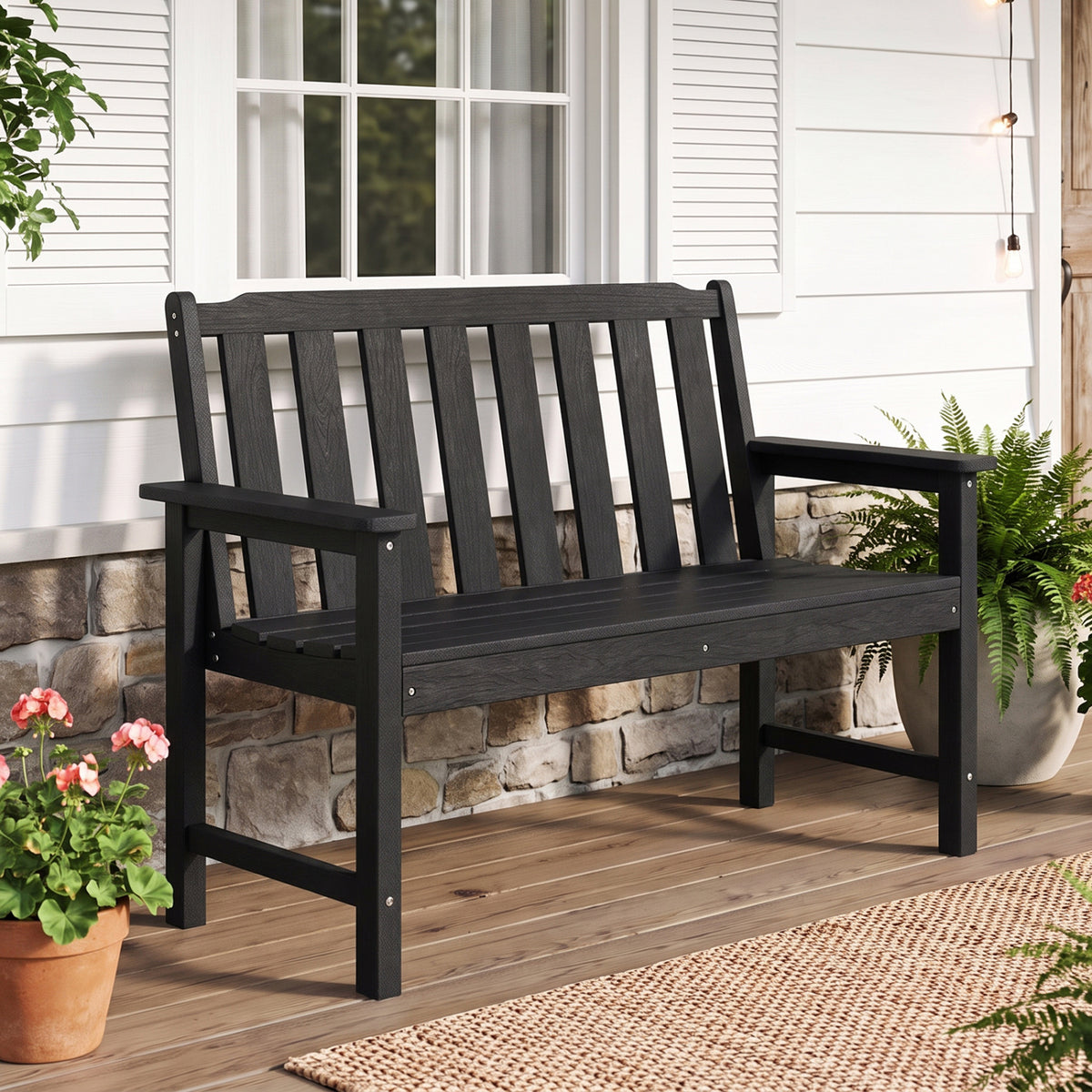 Black slatted garden bench with armrests on a wooden porch beside potted flowers.