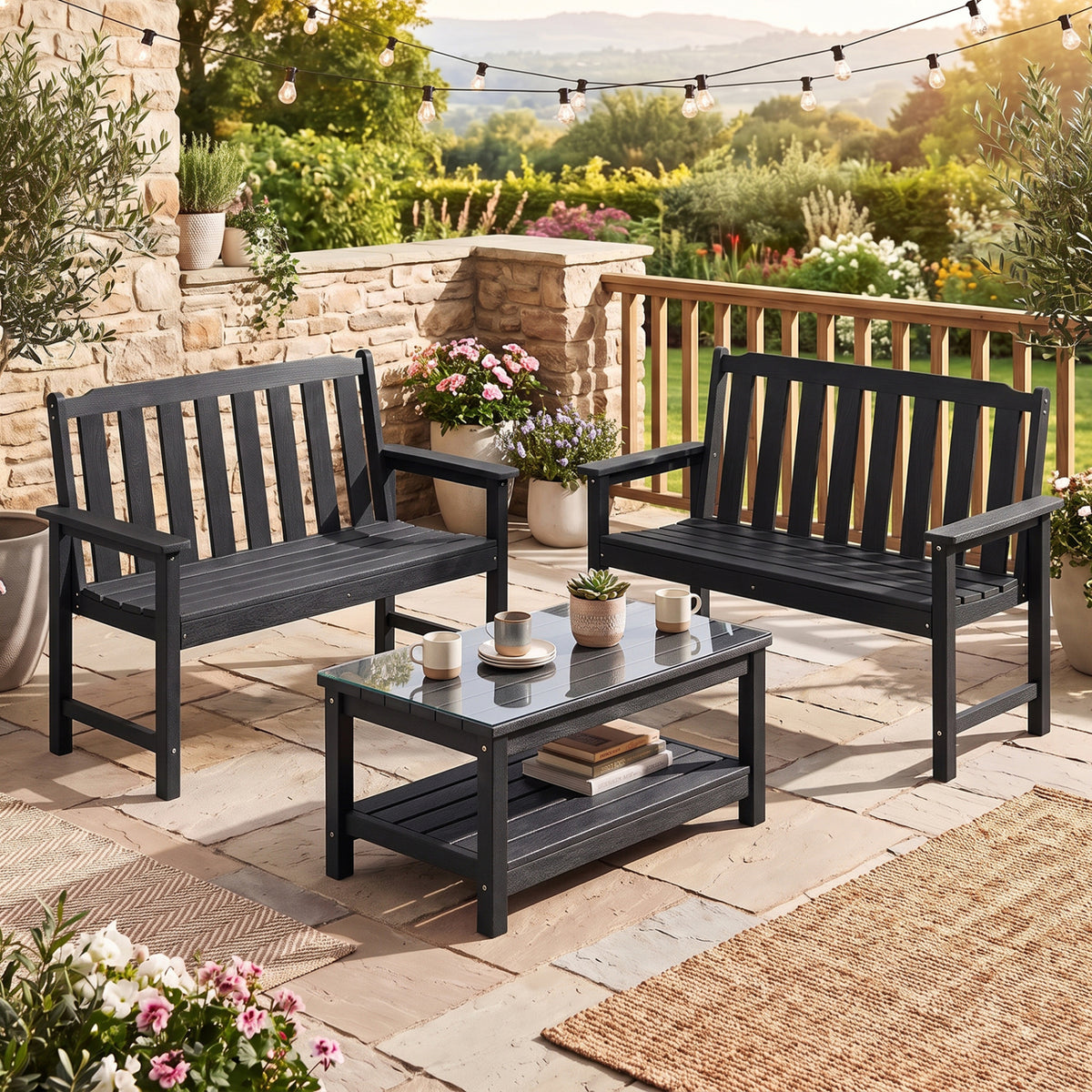 Two black garden benches and a low matching table arranged on a stone patio.