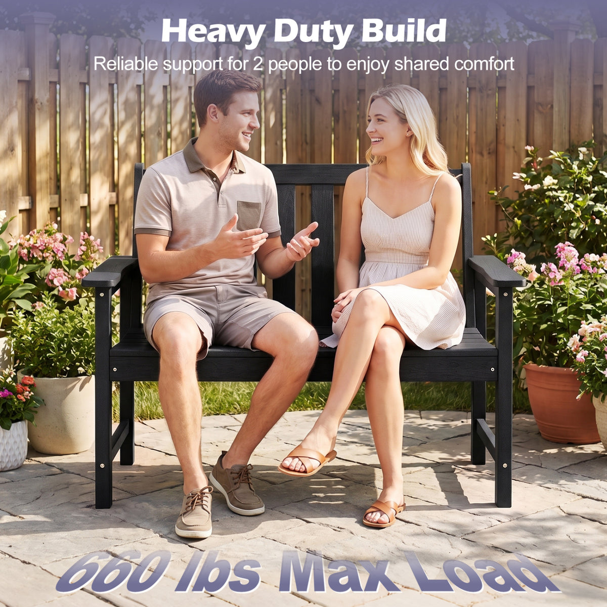A couple sits together on a black garden bench with armrests on a paved patio.