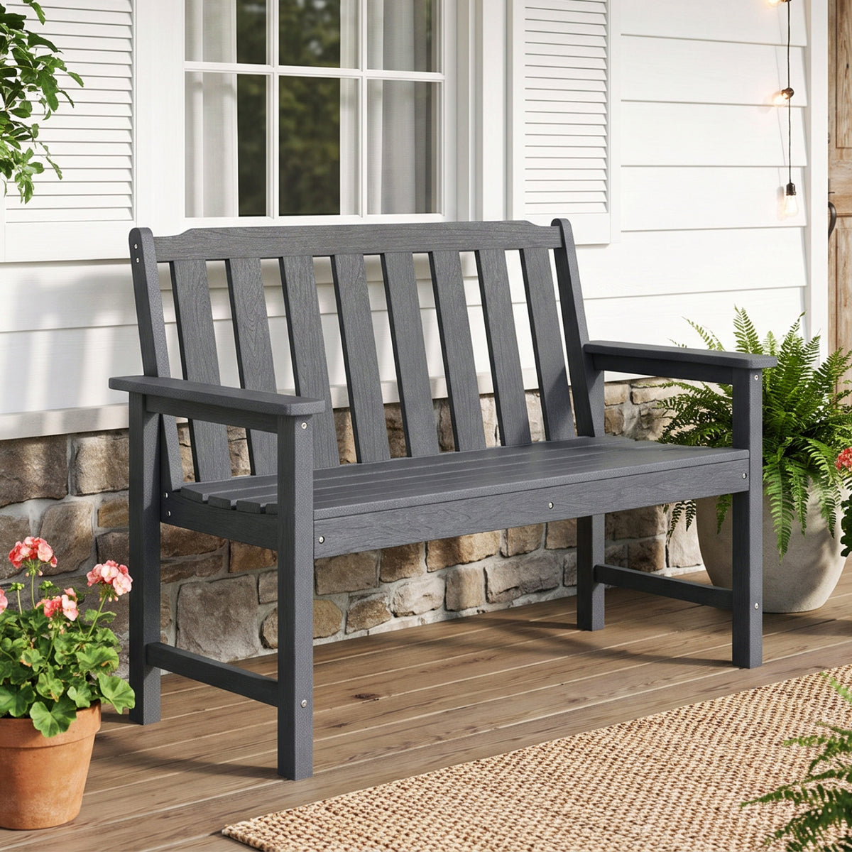 A charcoal slatted bench with a tall backrest and armrests stands on a wooden porch.
