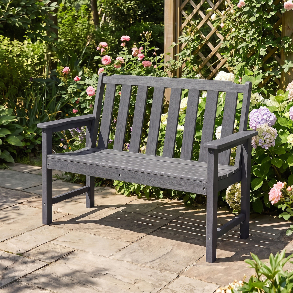 A dark gray slatted bench with a backrest and armrests stands on a garden patio.