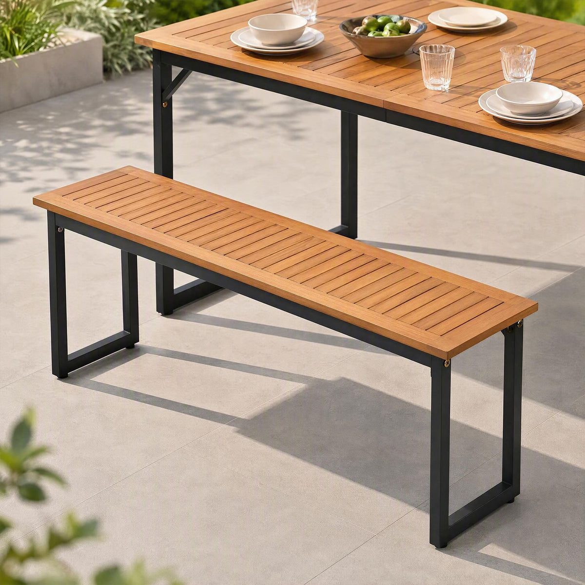 Slatted bench beside a dining table set with plates, glasses, and a bowl of fruit.