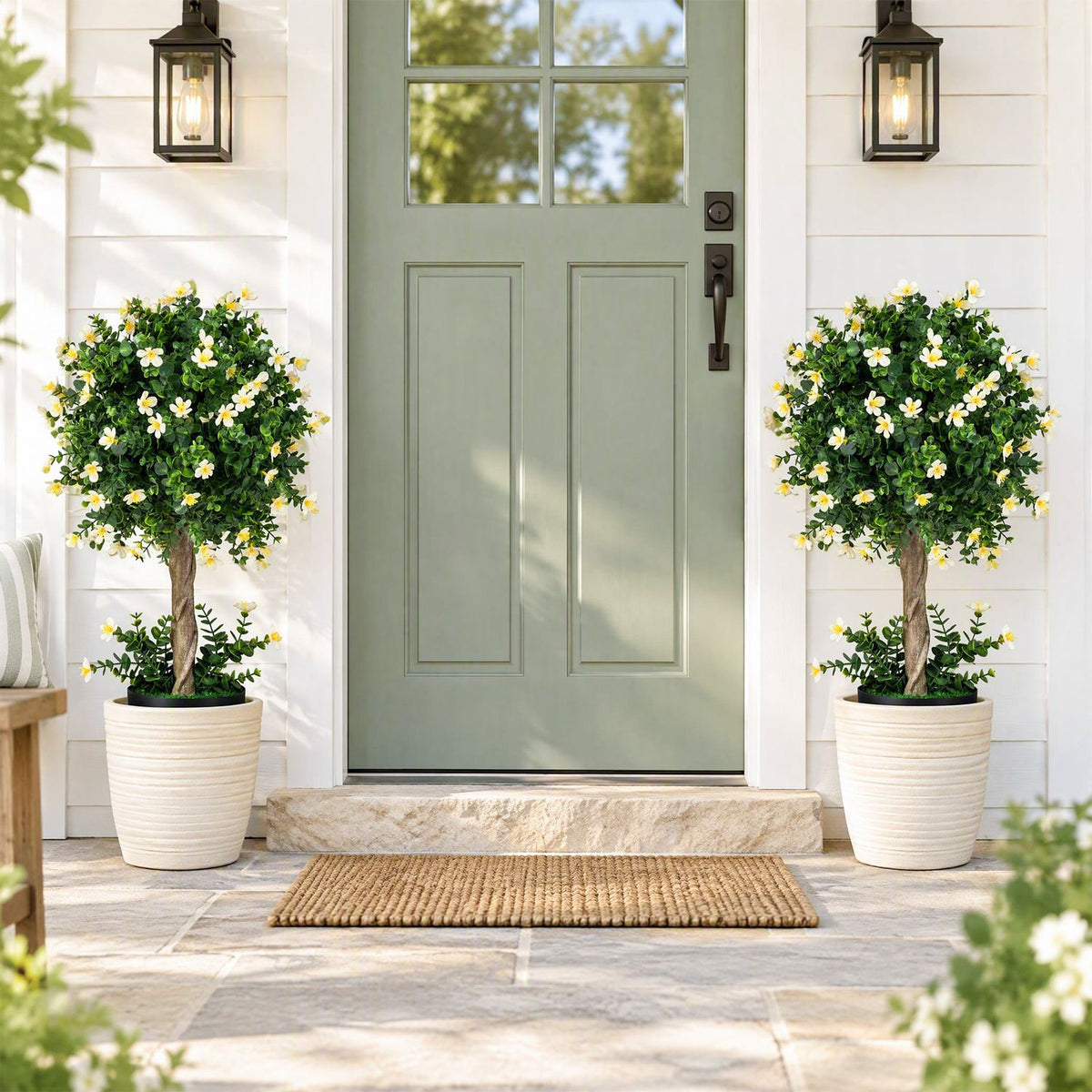 Two flowering topiary trees in white pots flank a pale green front door.