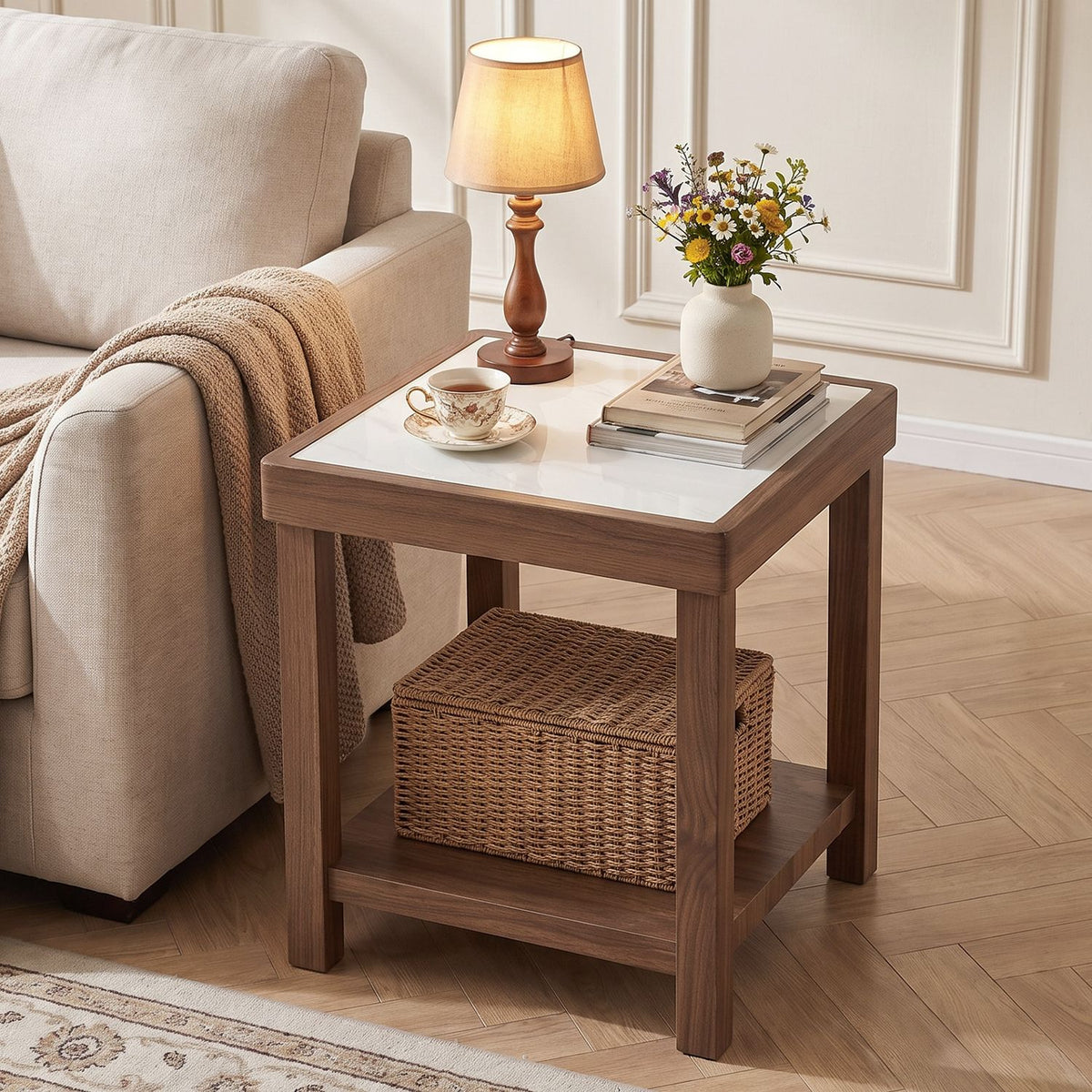 Square brown side table with a white top beside a beige sofa, styled with a lamp, flowers and a woven basket.