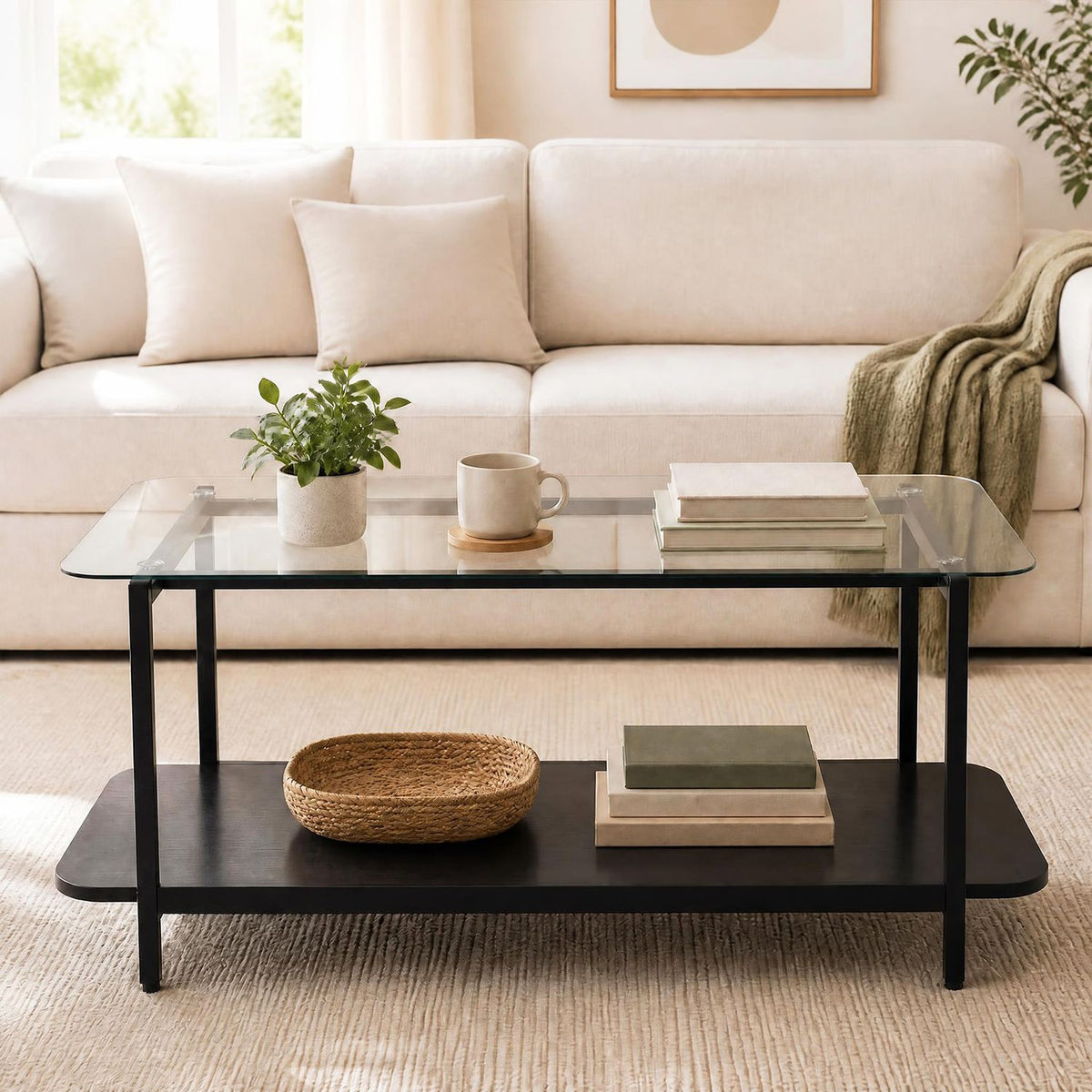 Black two-tier glass coffee table styled with books and decor in front of a cream sofa