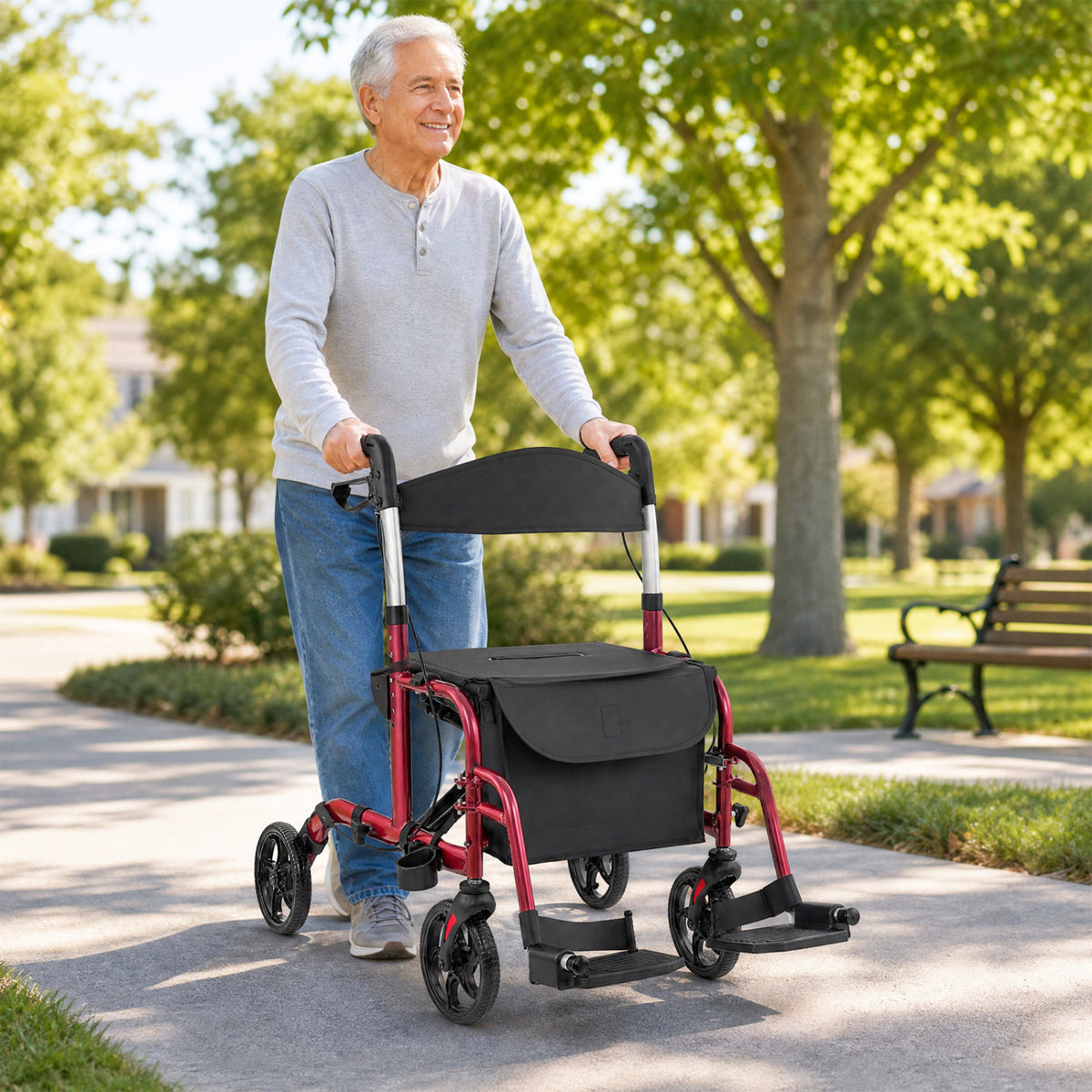 Older man pushing a red-framed rollator with a black storage bag along a park path.