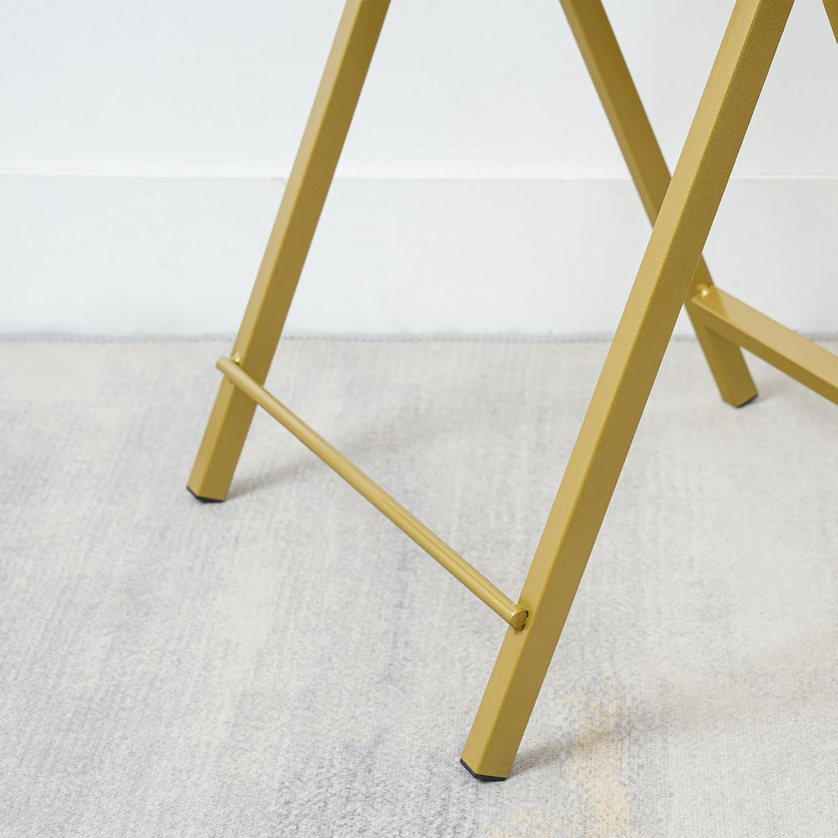 Close-up of the gold metal X-frame and foot cap on the folding table against a light rug