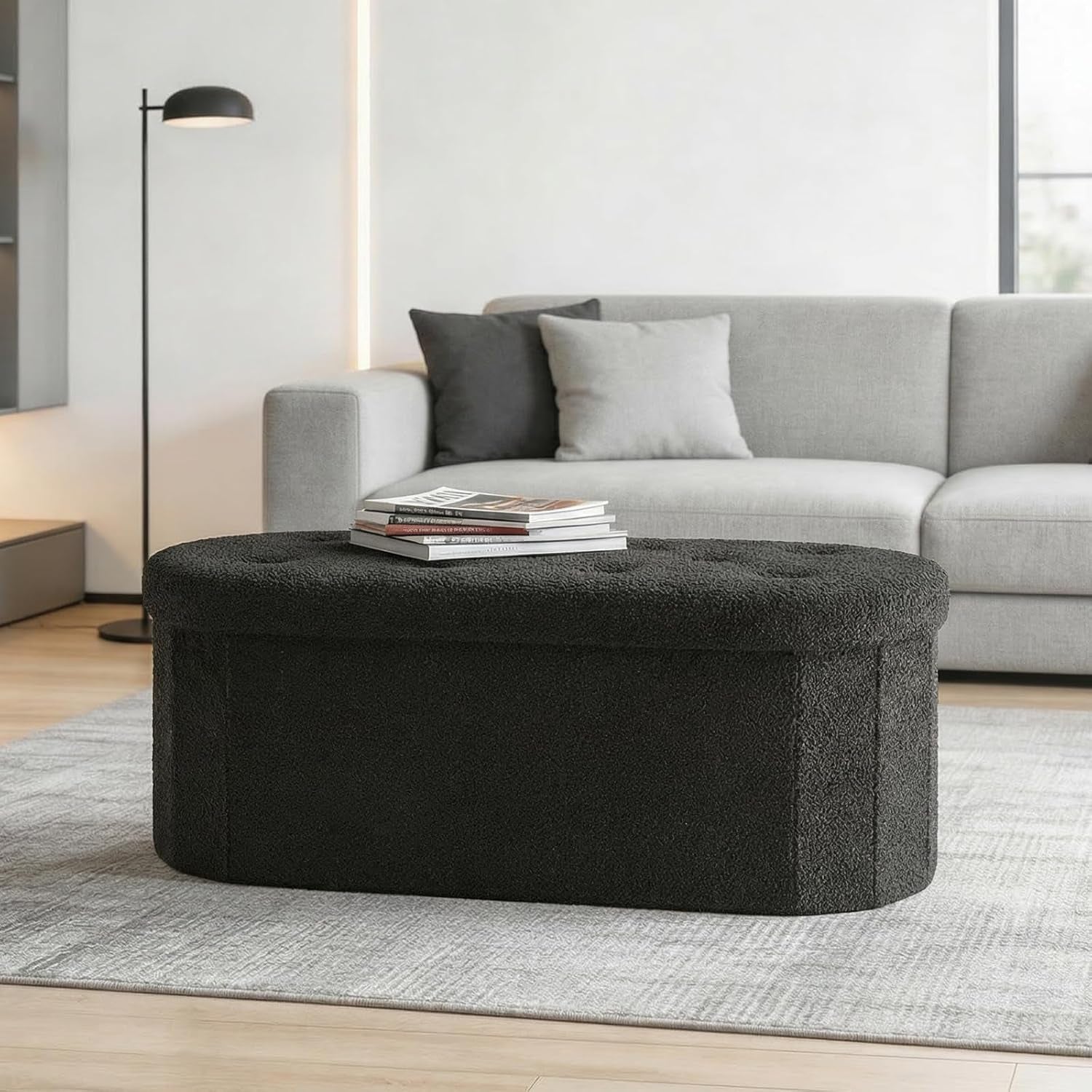 Black tufted oval storage bench used as a coffee table in a contemporary living room