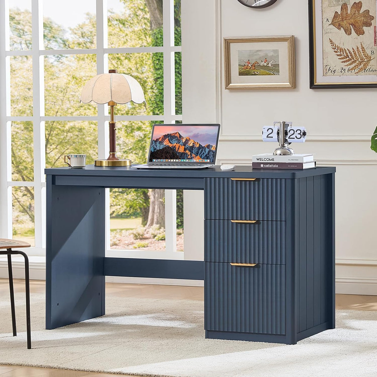 Navy blue desk angled view with laptop and lamp by a large window in a bright room