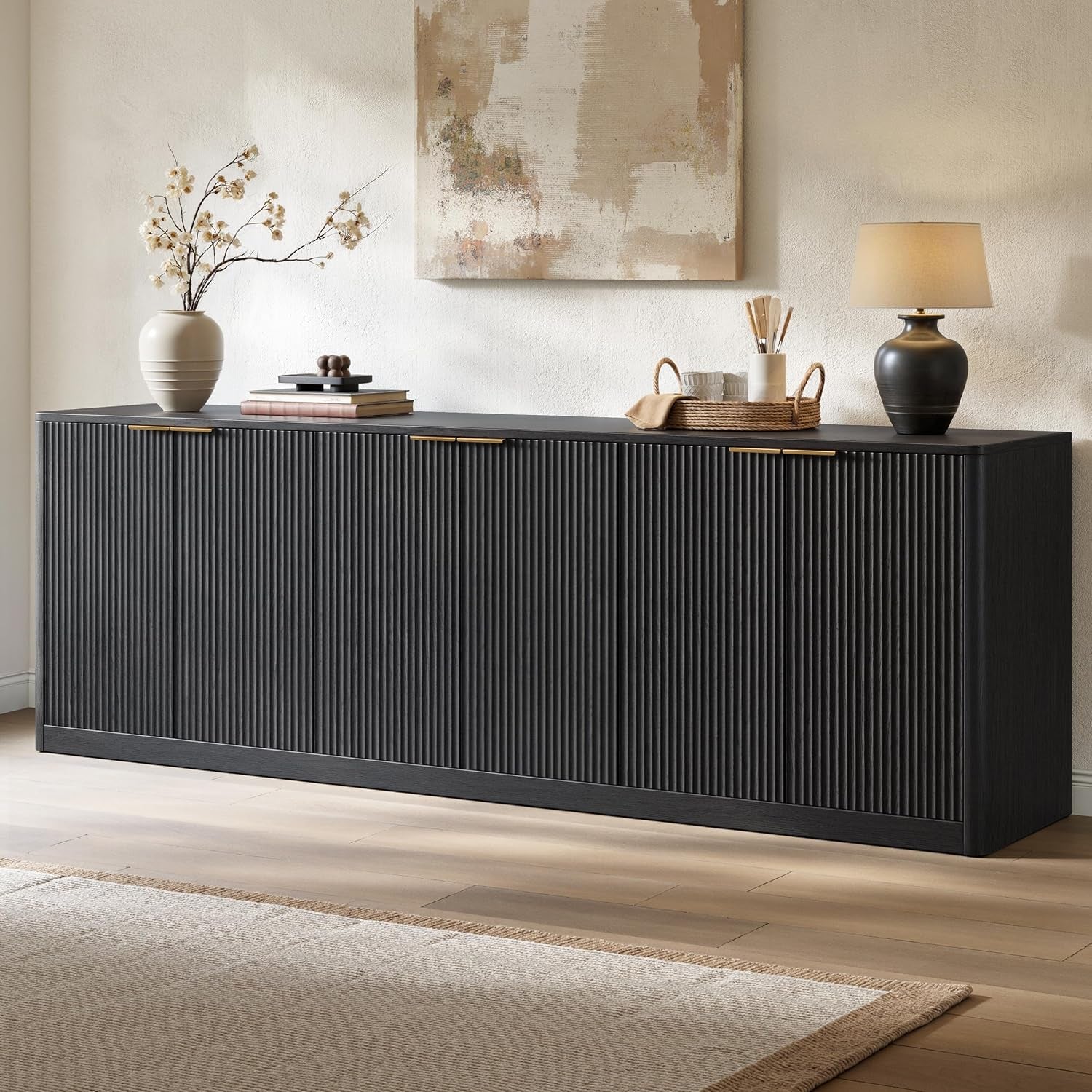 Long black fluted buffet in a neutral room styled with a lamp, vase, and tray of utensils.