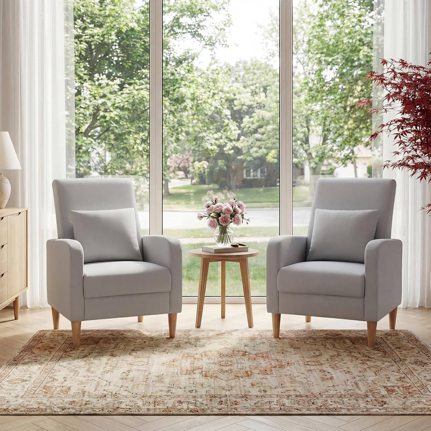 Pair of light gray high-back accent chairs with pillows flanking a small round table in front of a large window.