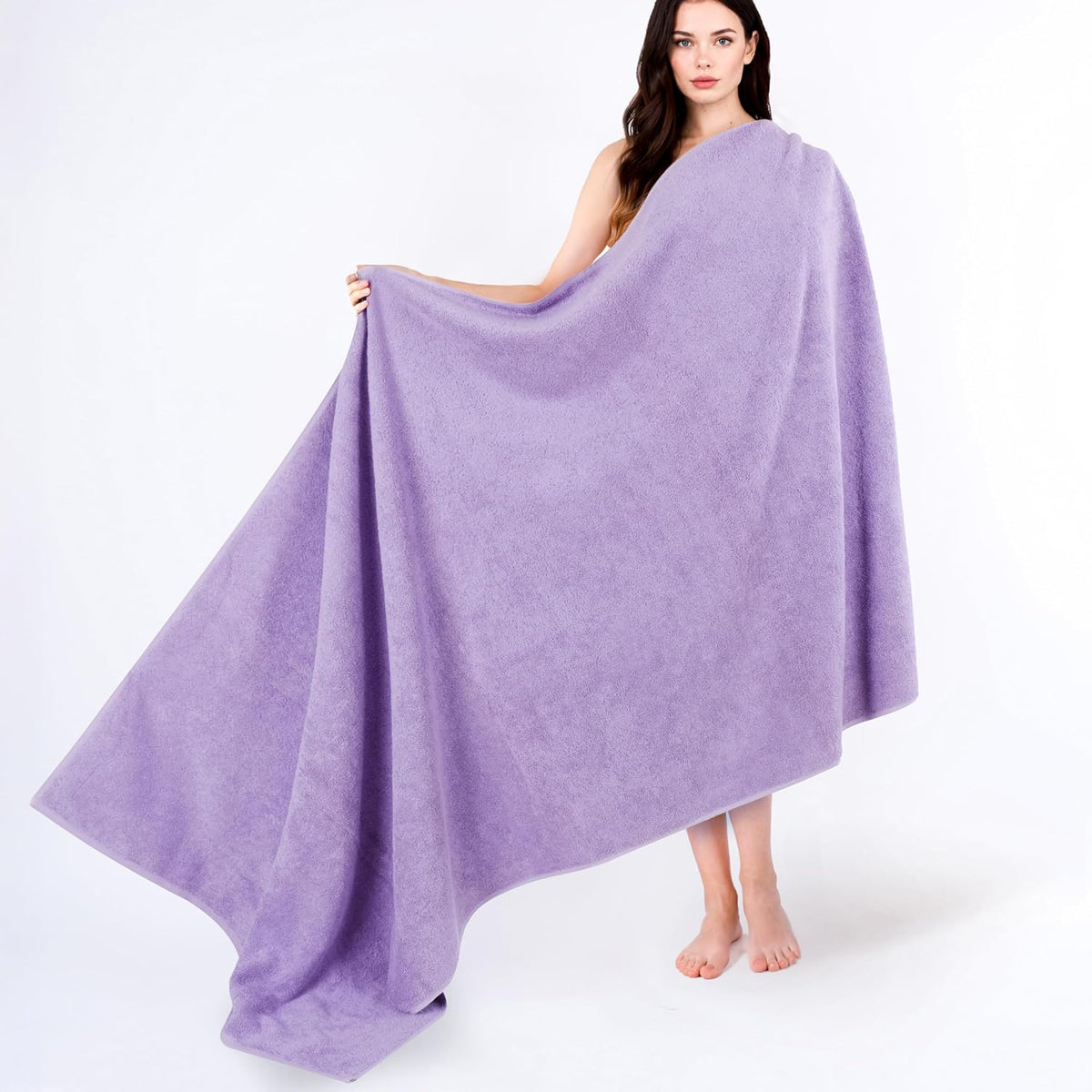 Model standing barefoot holding open a large lavender towel draped across her body