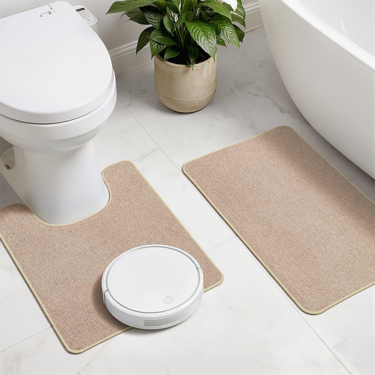 Beige U-shaped toilet rug and rectangular mat placed near tub and toilet with a white robot vacuum nearby