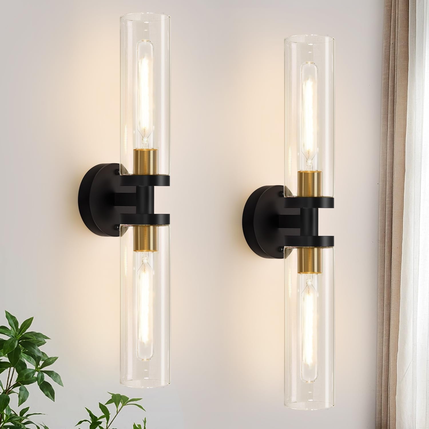 Pair of vertical black-and-gold wall sconces with clear cylindrical glass shades on a light wall.