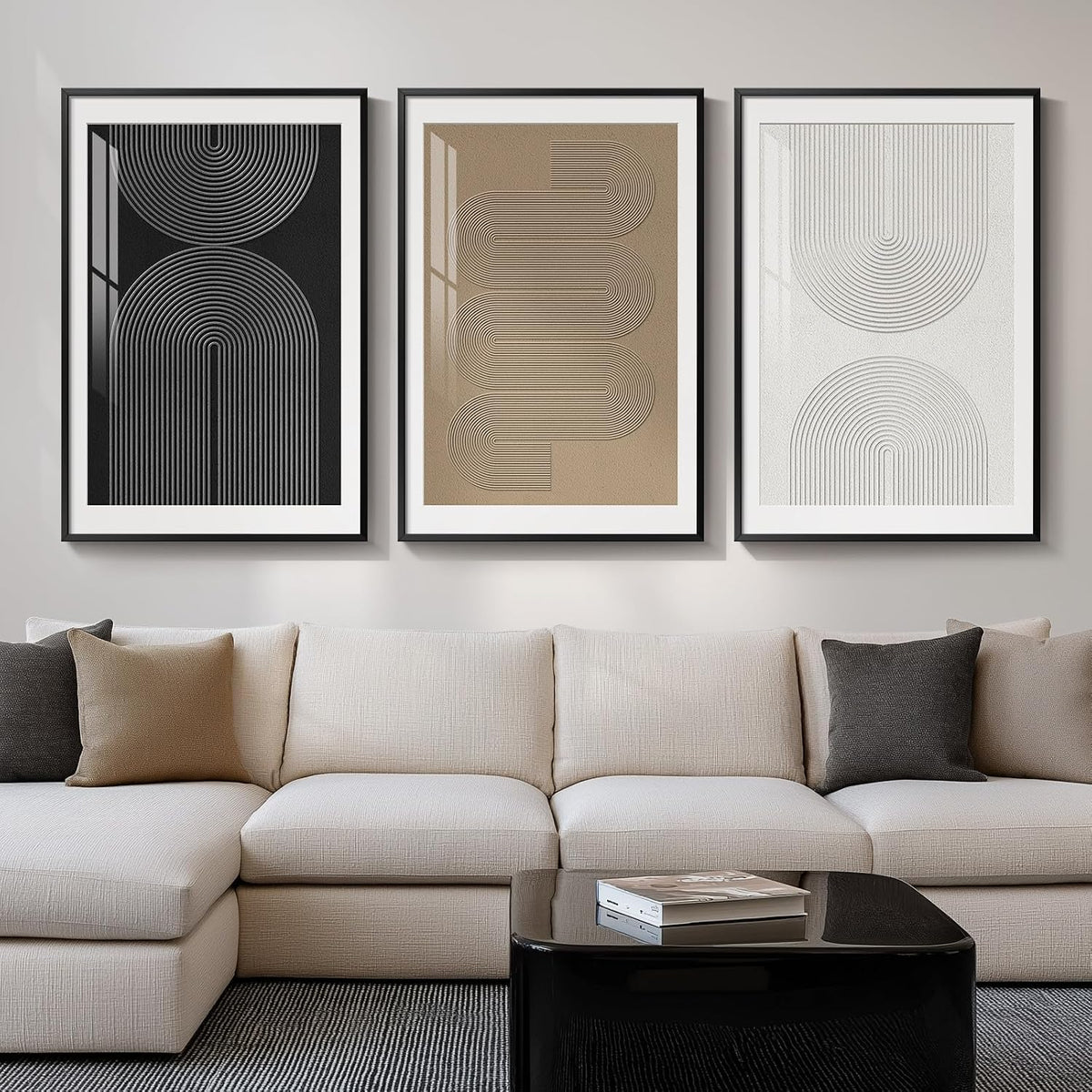 Three tall framed abstract line prints (black, tan, white) hung above a light sectional sofa.