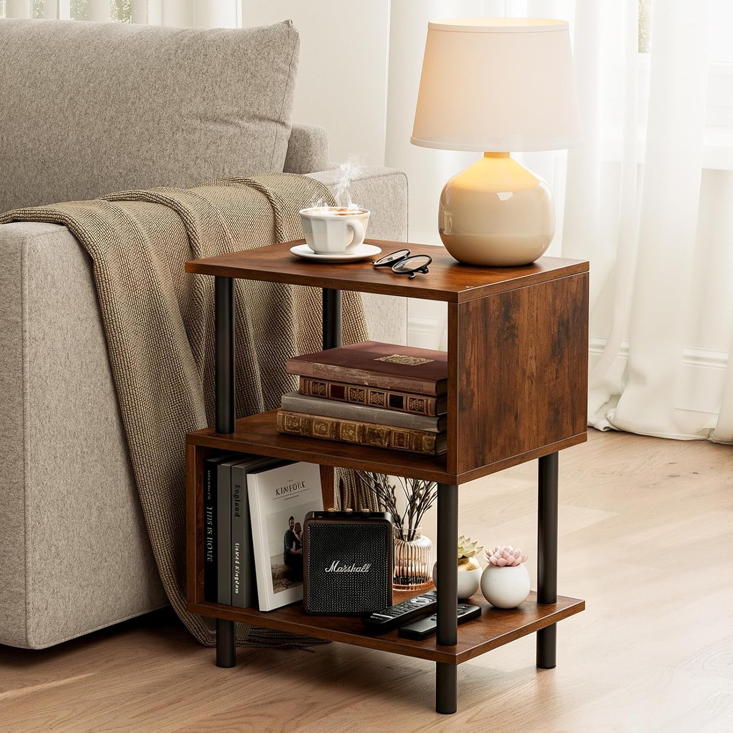 Rustic brown 3-tier side table next to a light grey sofa with lamp and cup on top, angled front view