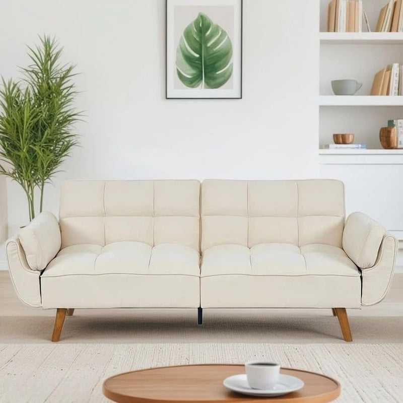 Cream-colored convertible sofa with tufted seat and rolled arm pillows in a minimalist living space.