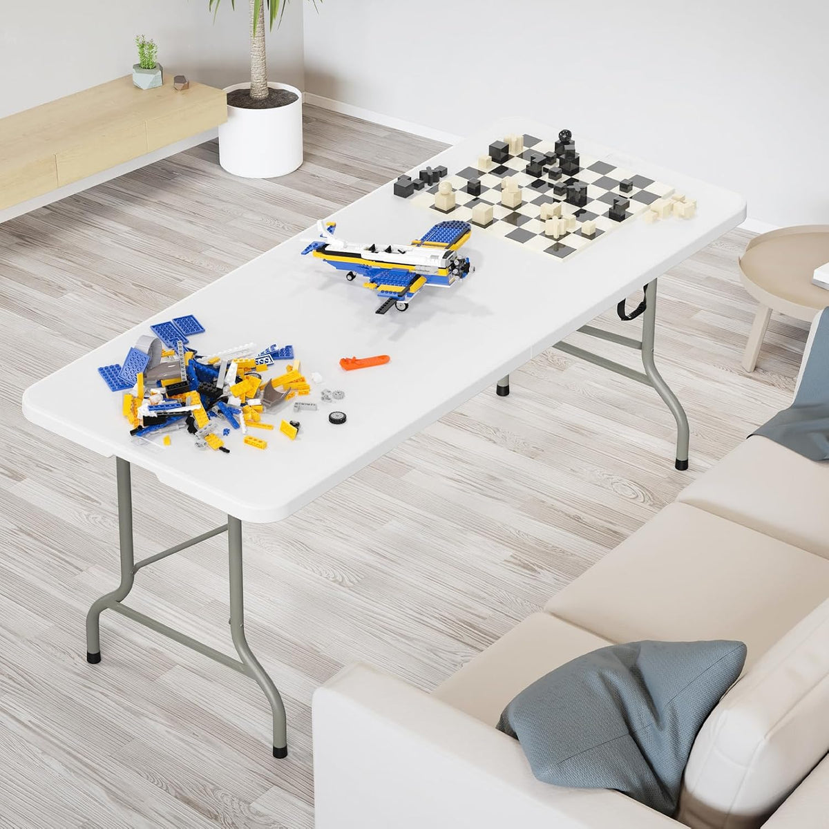 White folding table set up indoors with a toy airplane, scattered building bricks and a chess set.