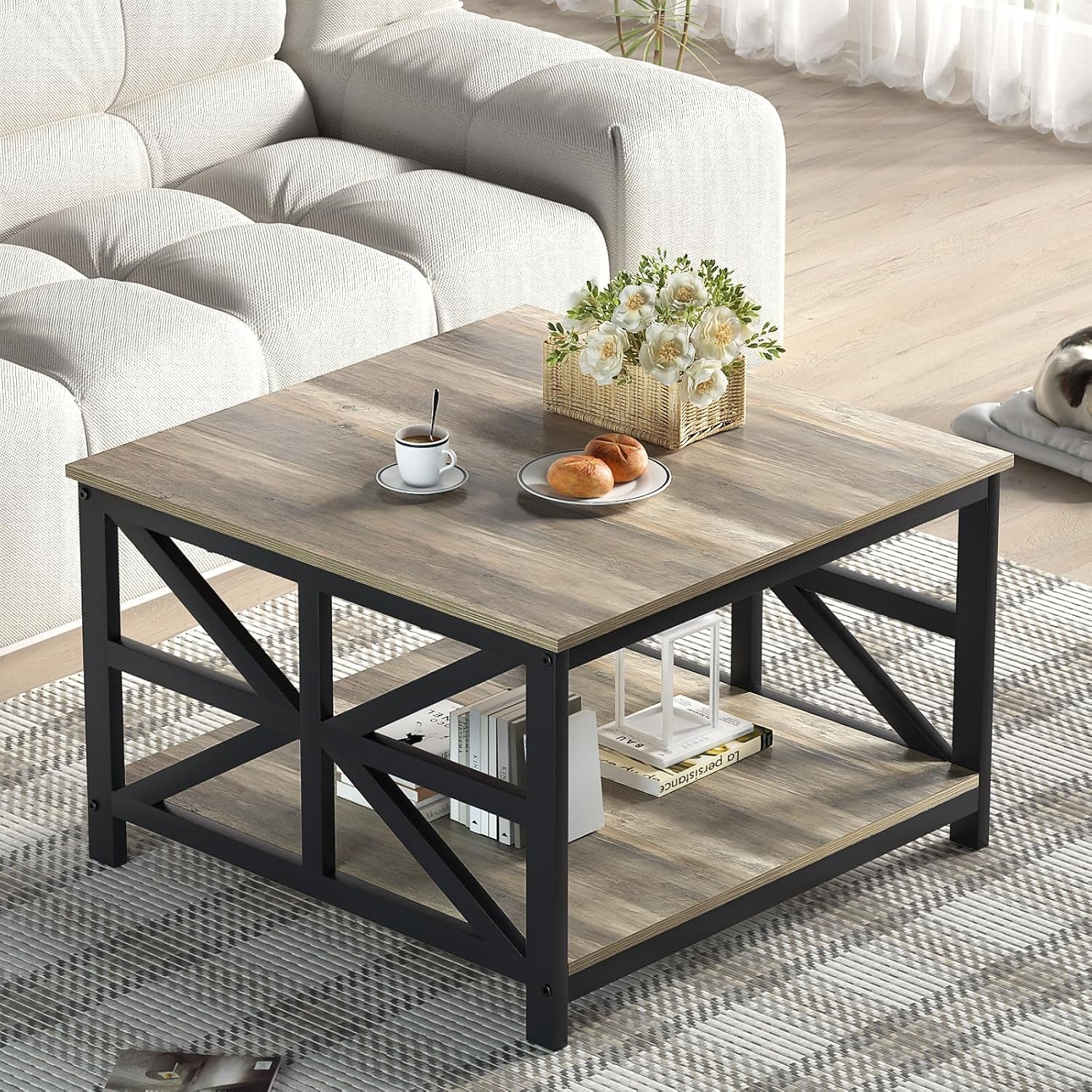 Square-view of the table near a tufted light sofa showing wood grain top, lower shelf and metal cross braces.