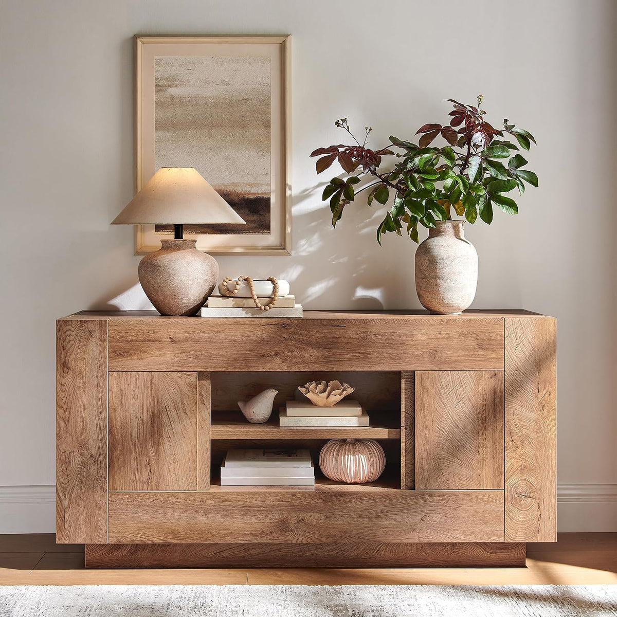 Honey-toned wood media console styled with a lamp, books and a vase of greenery