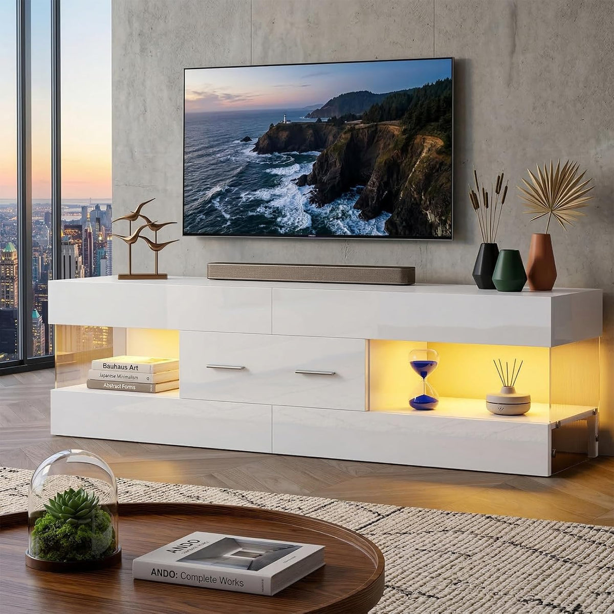 White glossy TV stand with lit side cubbies, flat-screen above, decorative vases and coffee table in foreground