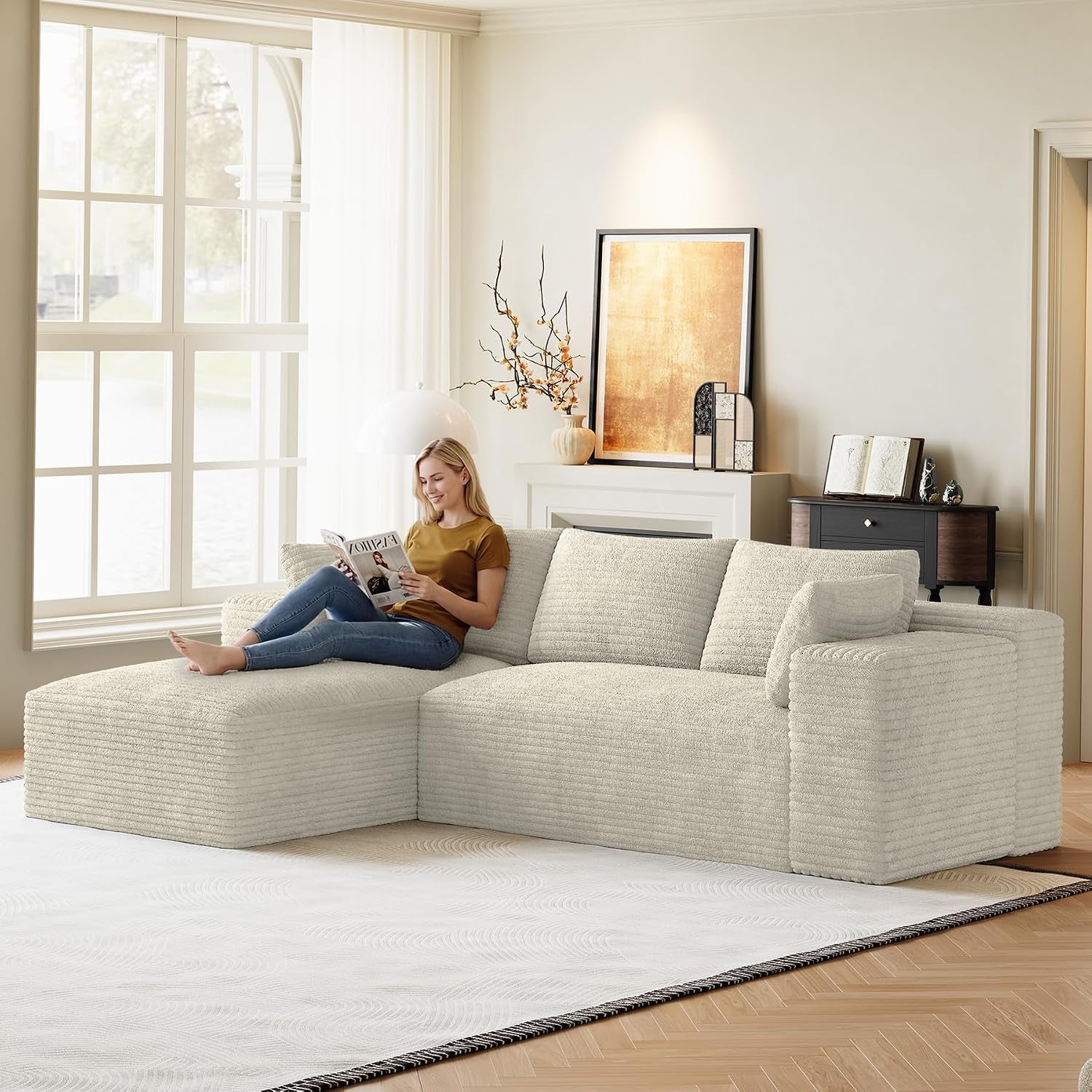 Light cream L-shaped modular sectional with chaise in a bright living room, woman reclining reading a magazine