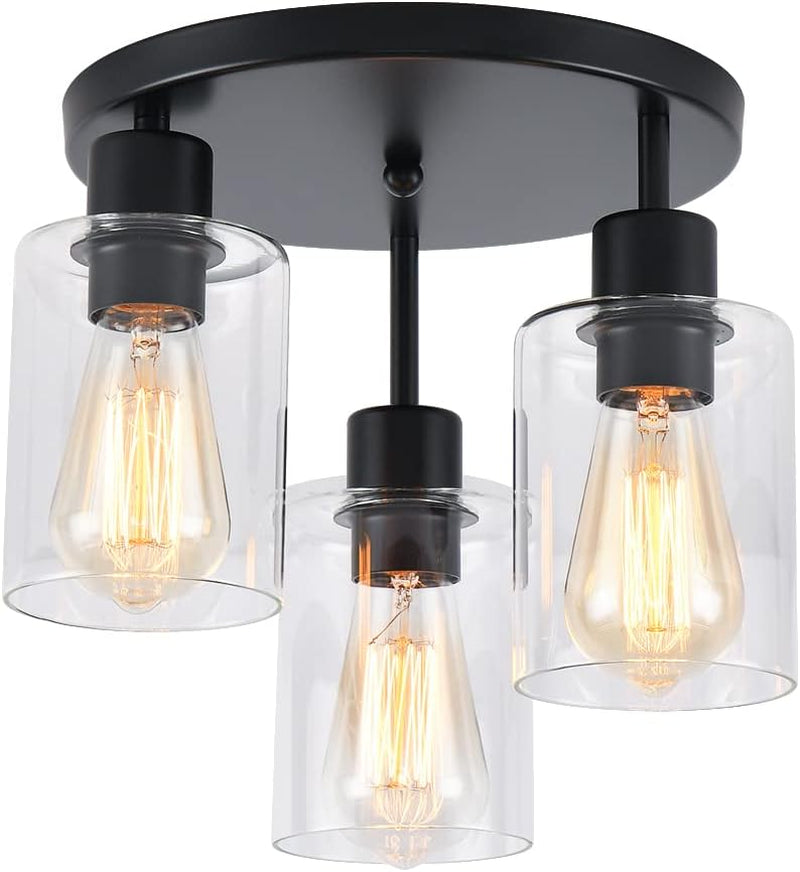 Close frontal product shot of a three-light black semi-flush ceiling fixture with clear cylindrical glass shades and glowing