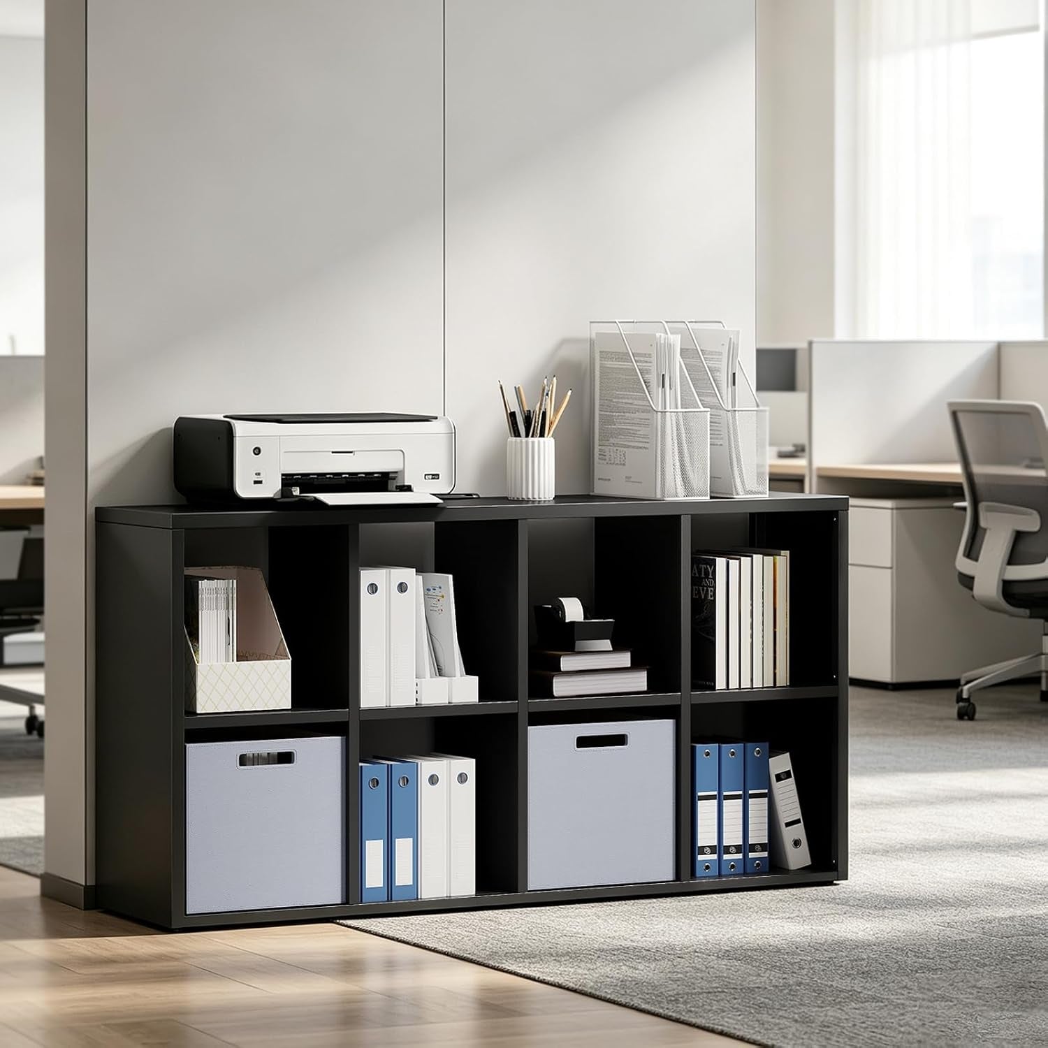 Black cube bookshelf positioned in a modern office with a printer, desk organizers on top and binders and fabric bins inside