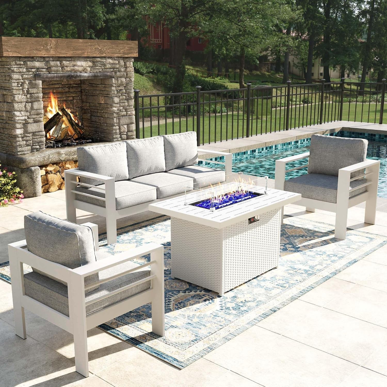 White-framed seating set with light gray cushions grouped around a white woven fire pit table by the pool.