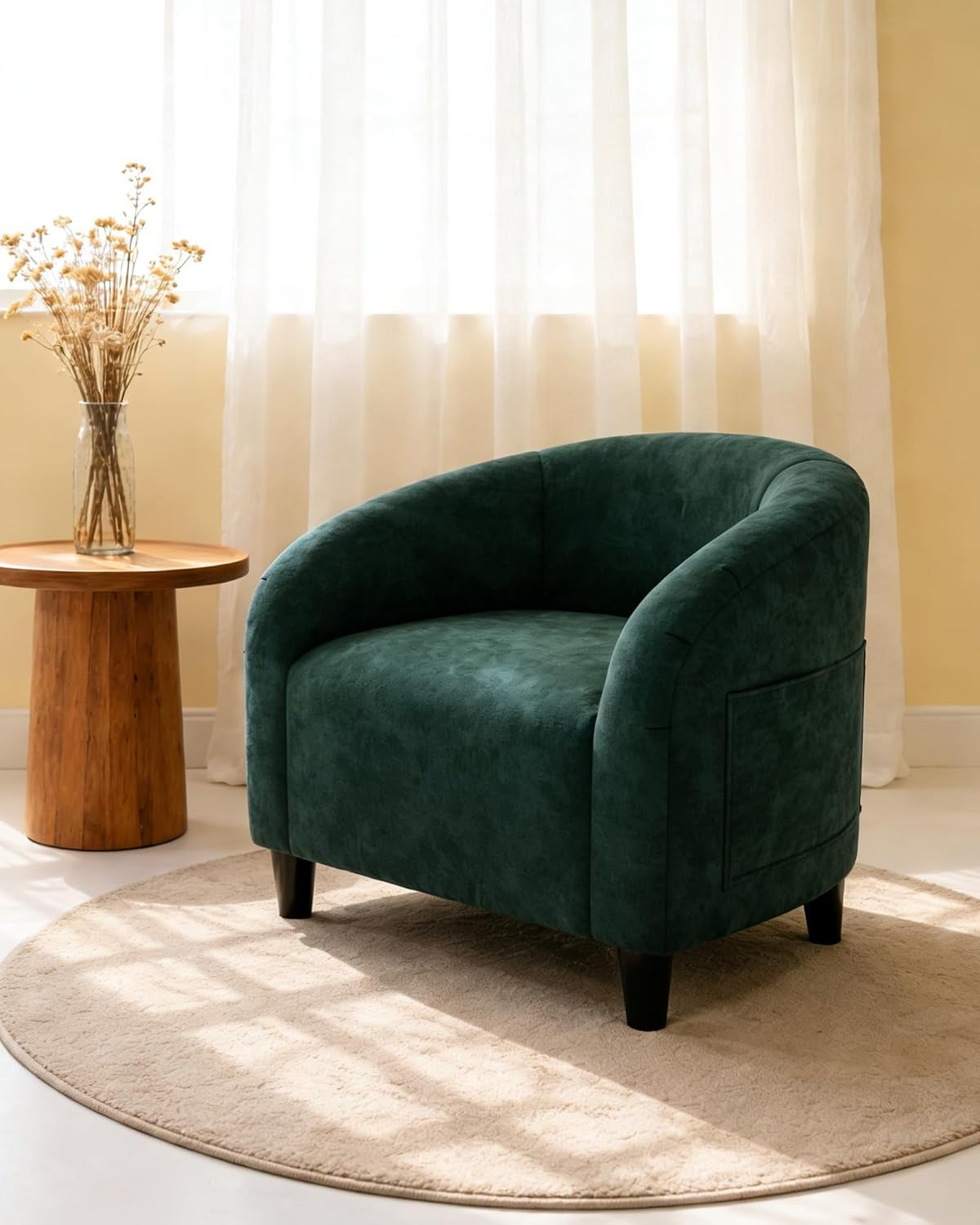Single dark green barrel chair on a round rug beside a wooden side table and vase by a sunlit window.