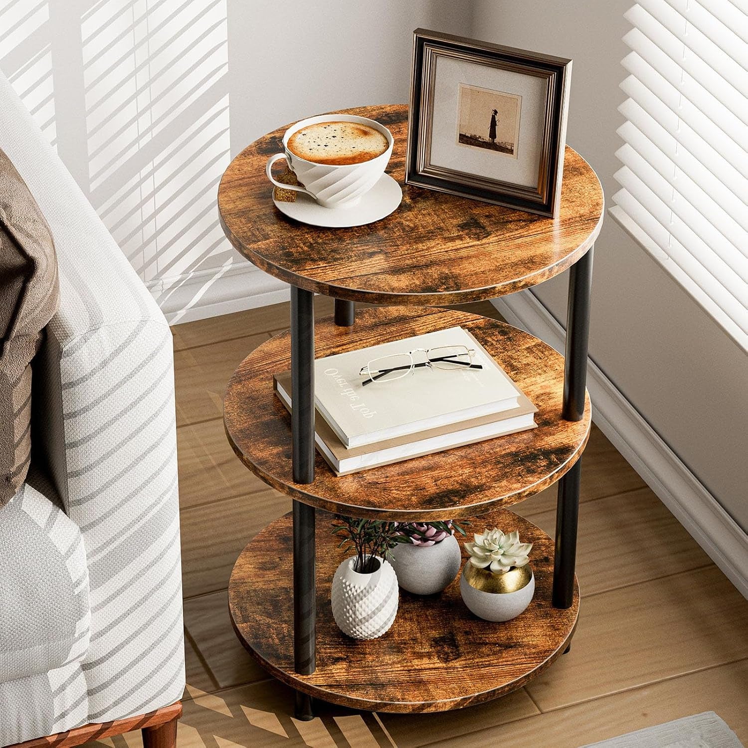 Round three-tier side table in rustic brown finish shown next to a sofa with coffee and framed photo on top shelf
