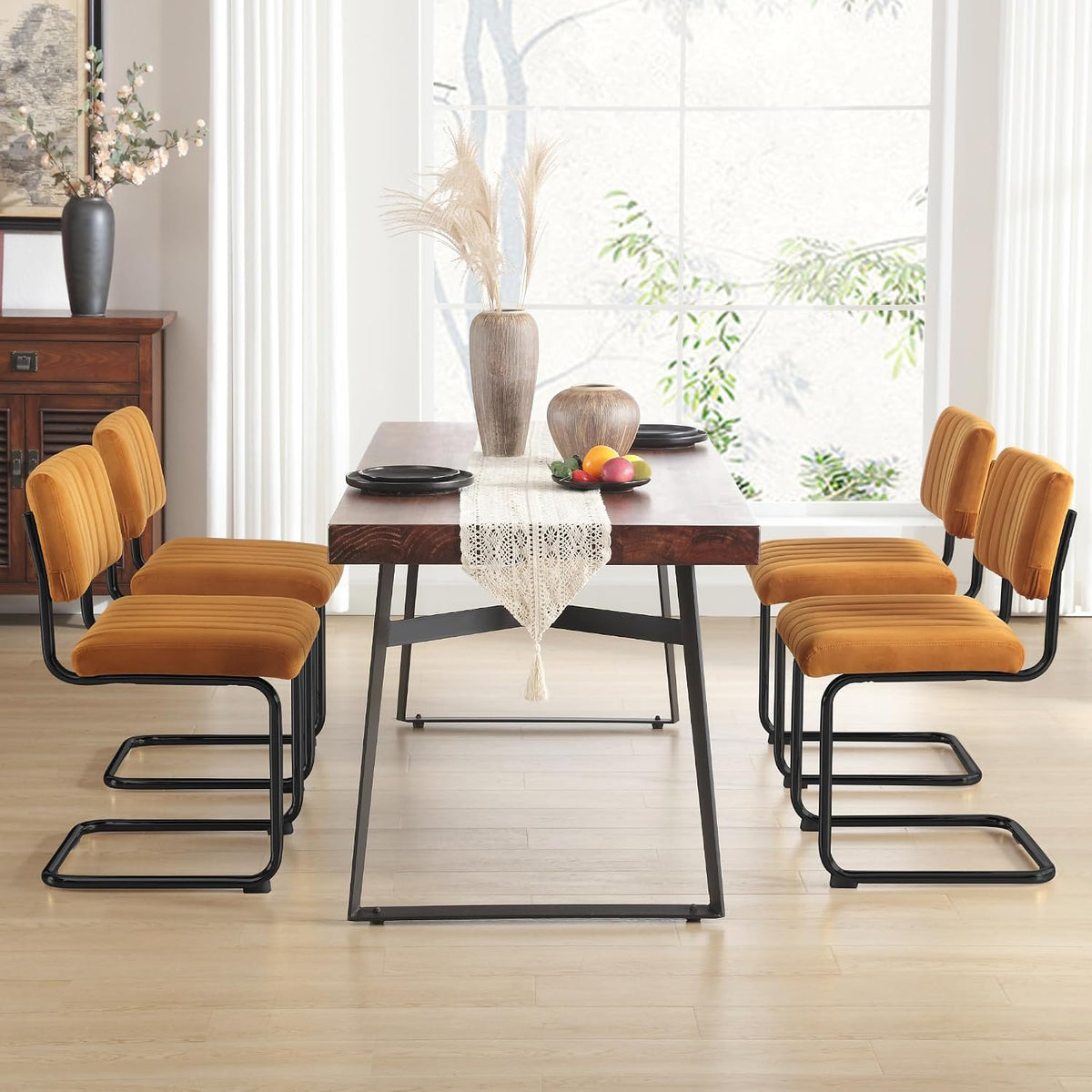 Six mustard velvet cantilever chairs arranged three on each side of a wood table in a bright dining room