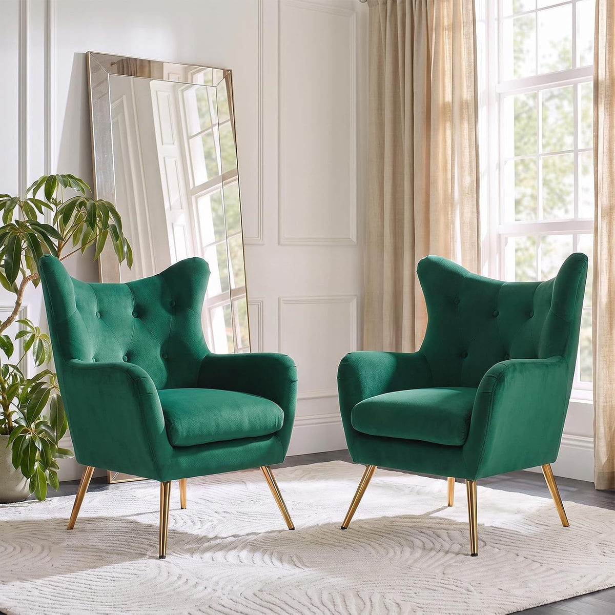 Pair of matching green velvet wingback chairs arranged facing slightly toward each other in a bright room.