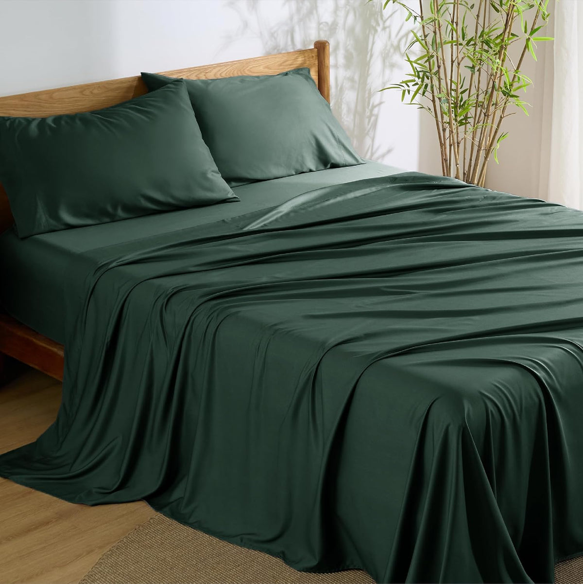 Bedroom shot of a bed dressed in deep forest green sheets and two matching pillowcases
