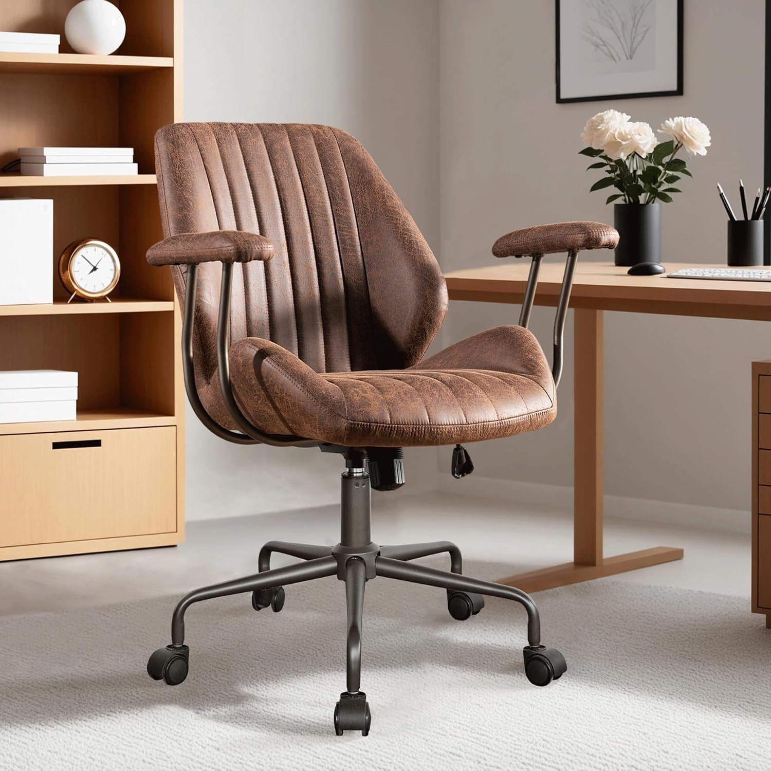 Front-facing brown faux-suede chair with stitched channels and metal base, shown next to a desk with a vase of flowers.