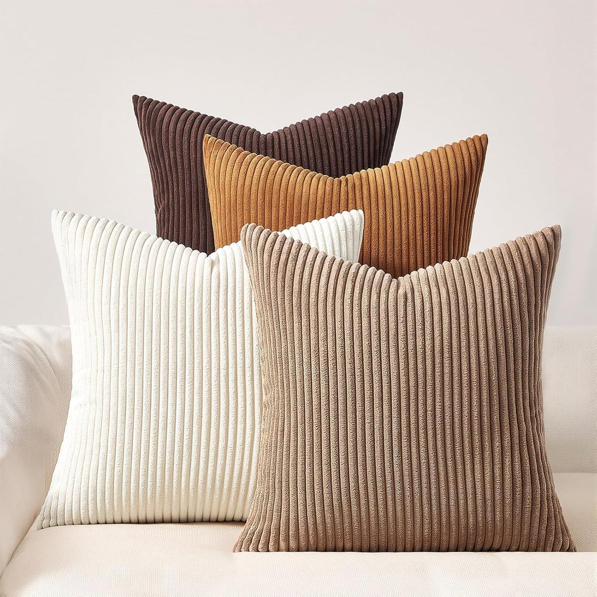 Five vertically-ribbed square pillows in brown, tan and cream arranged on a light sofa.
