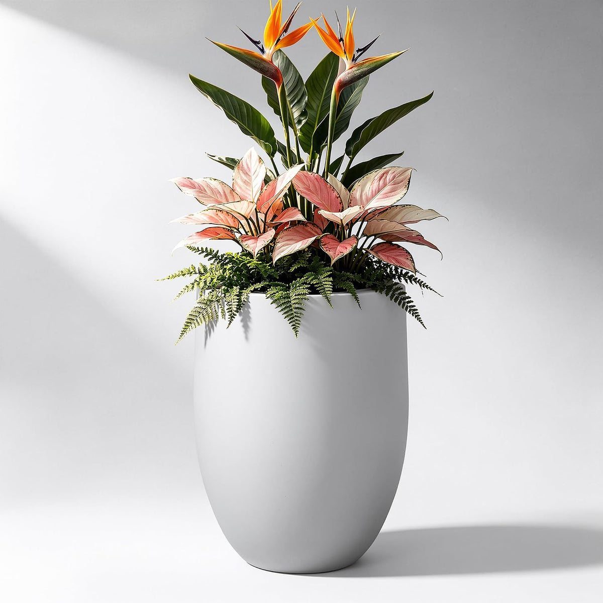 Tall light-gray planter filled with mixed plants including orange blooms and pink foliage against a neutral backdrop.