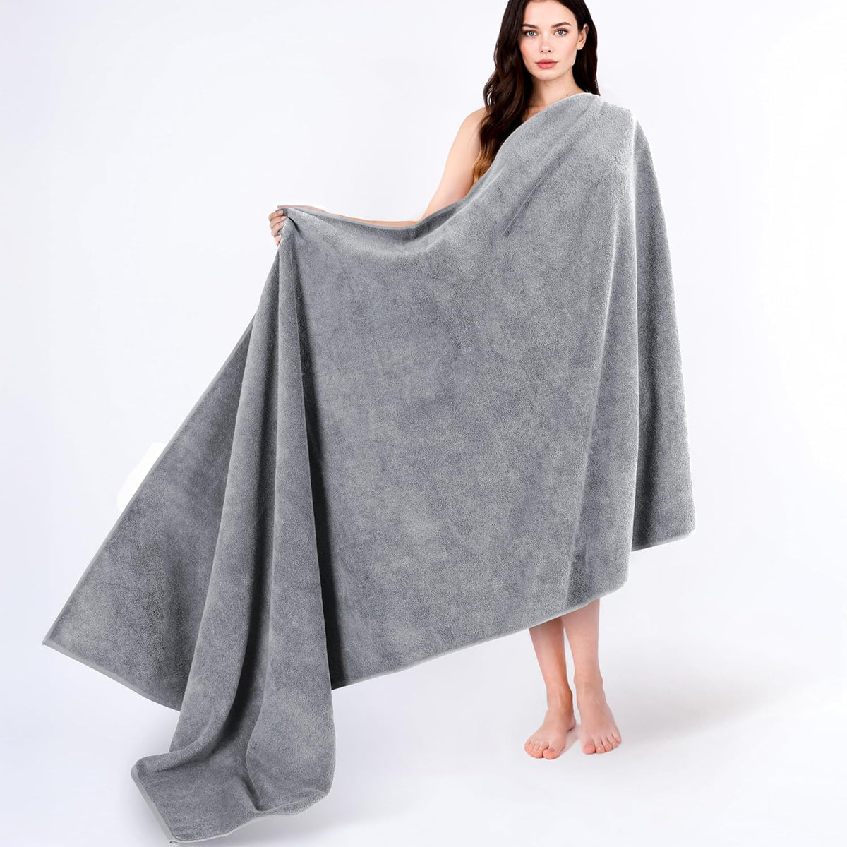 Woman holding a large soft gray towel spread wide to show its size and drape.