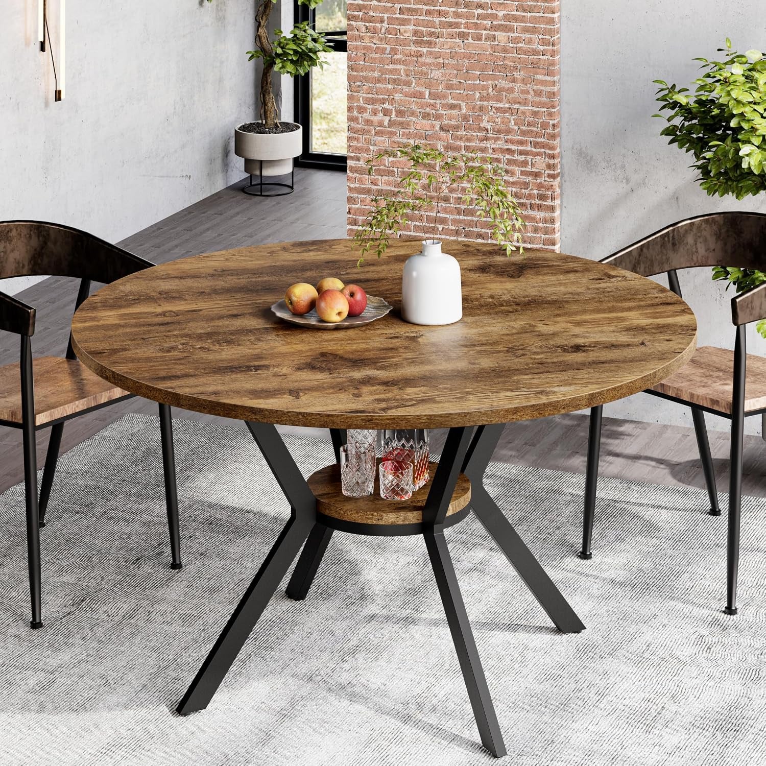 Rustic darker wood round table with black X-base and shelf, placed on a rug near exposed brick.