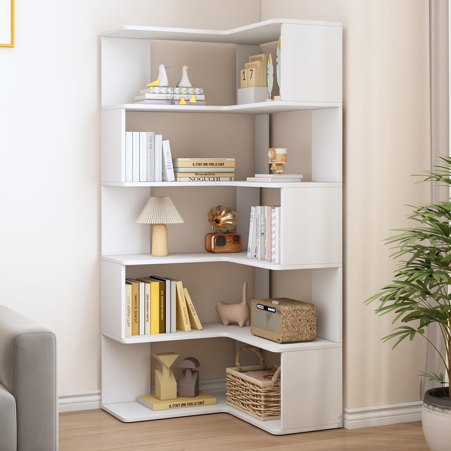 White corner bookshelf staged in a living room with plants, books and woven basket