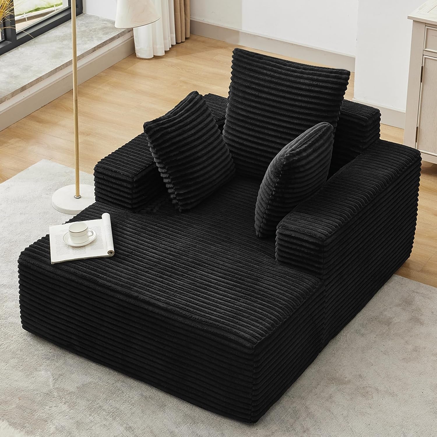 Top-down view of a black corduroy chaise with three ribbed pillows on a light rug and wood floor.
