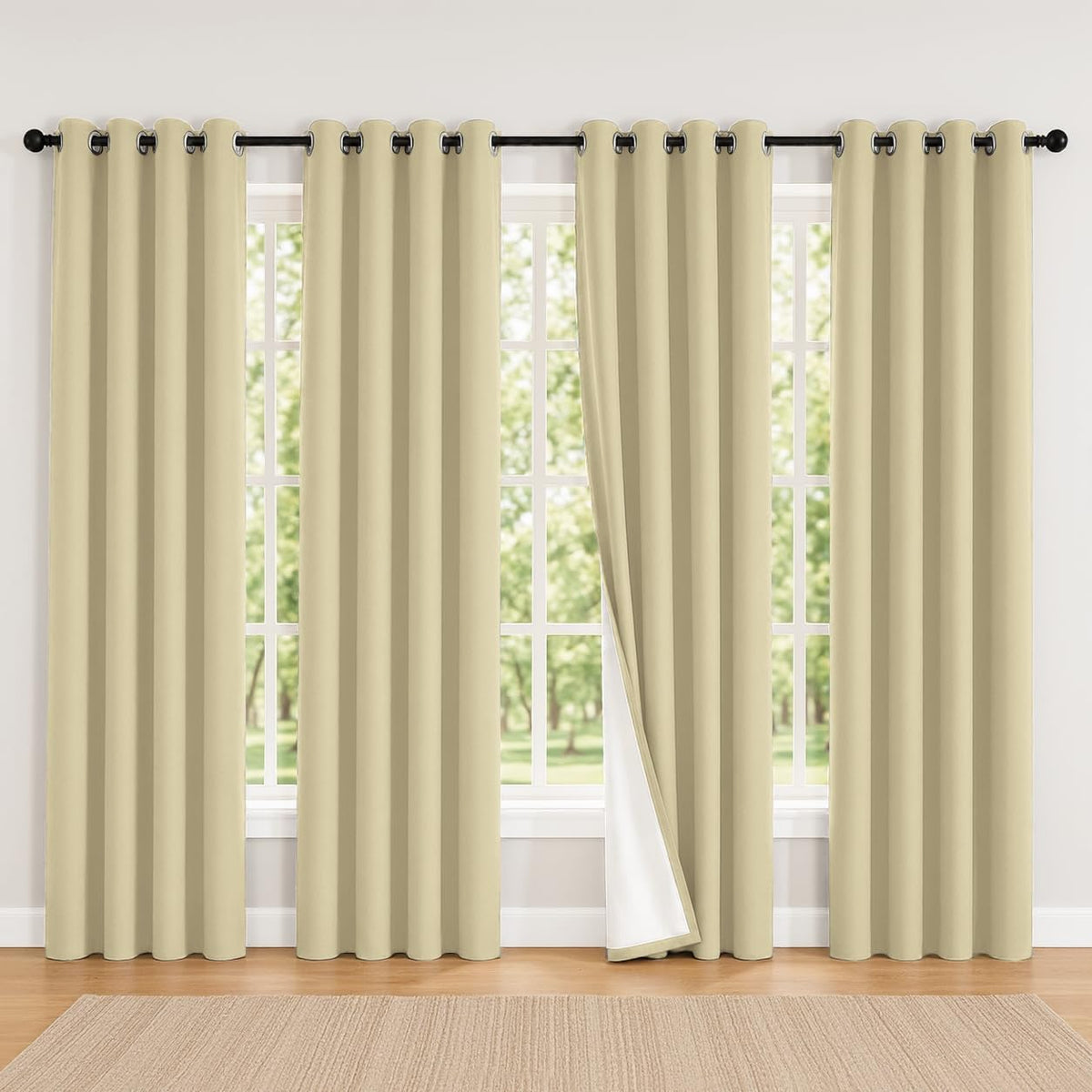 Wide window with four beige grommet curtain panels, one panel pulled to reveal white backing.