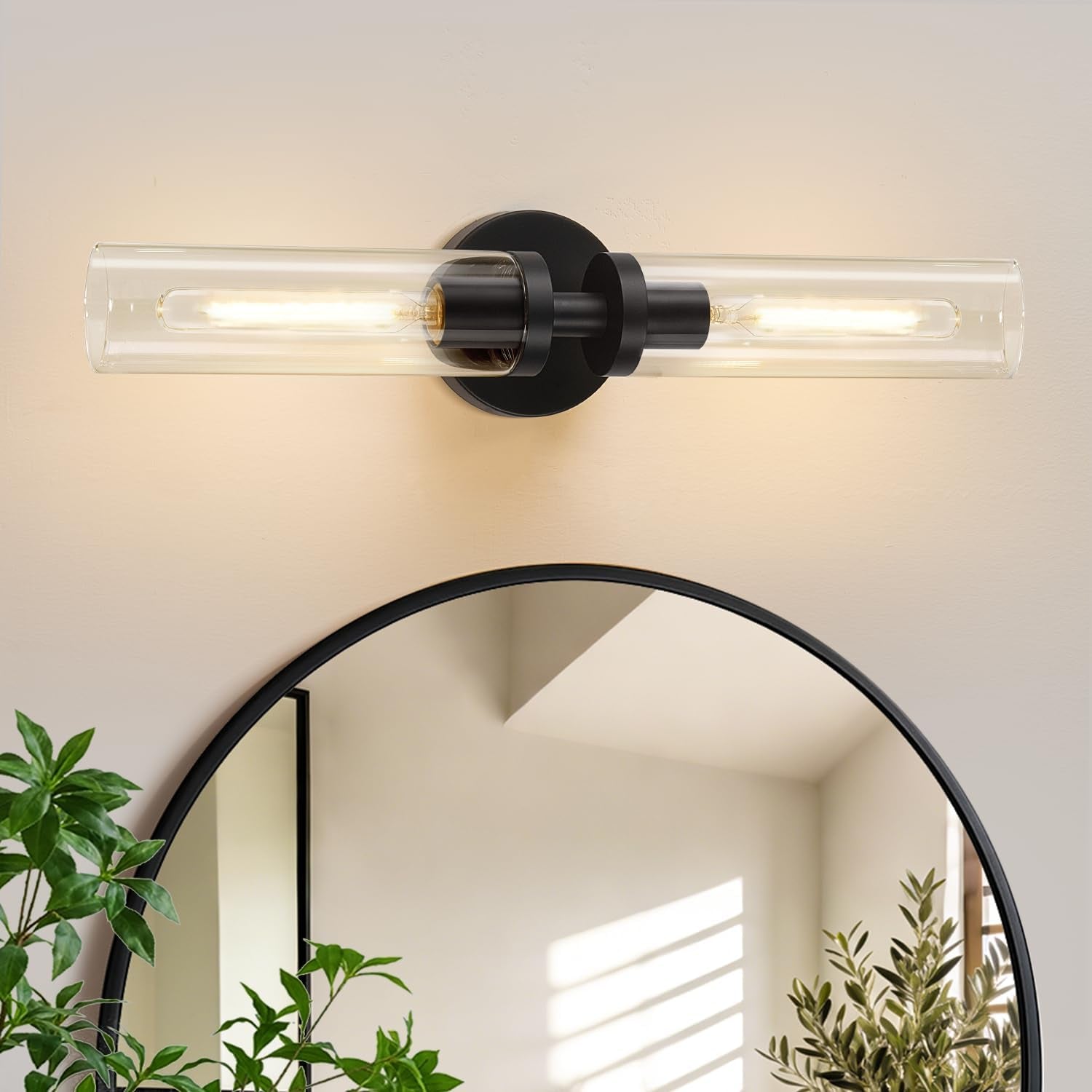 Single horizontal sconce mounted above a round mirror, showing clear glass tube and round black backplate.