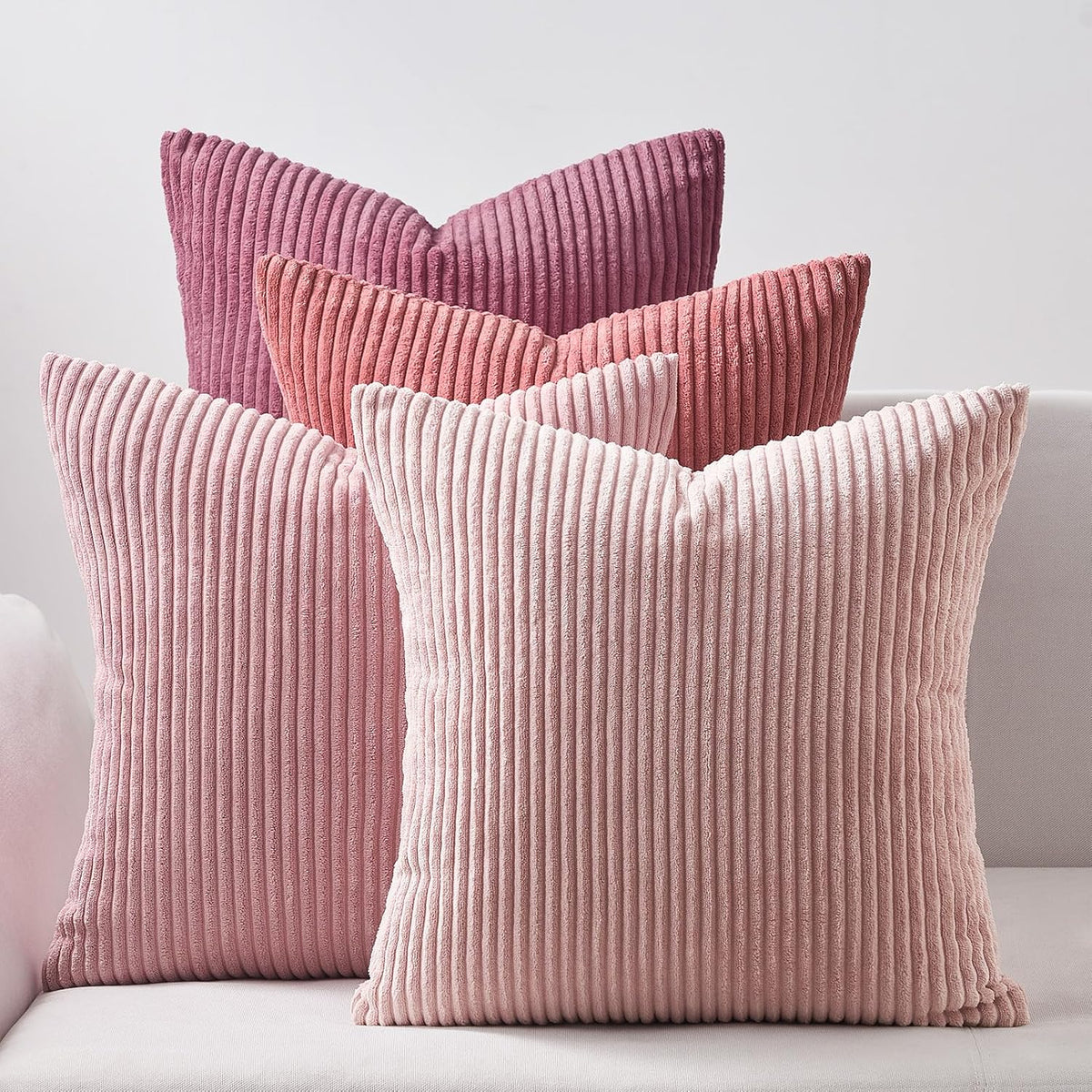 Four ribbed corduroy square pillows in varying pink tones arranged on a light sofa back
