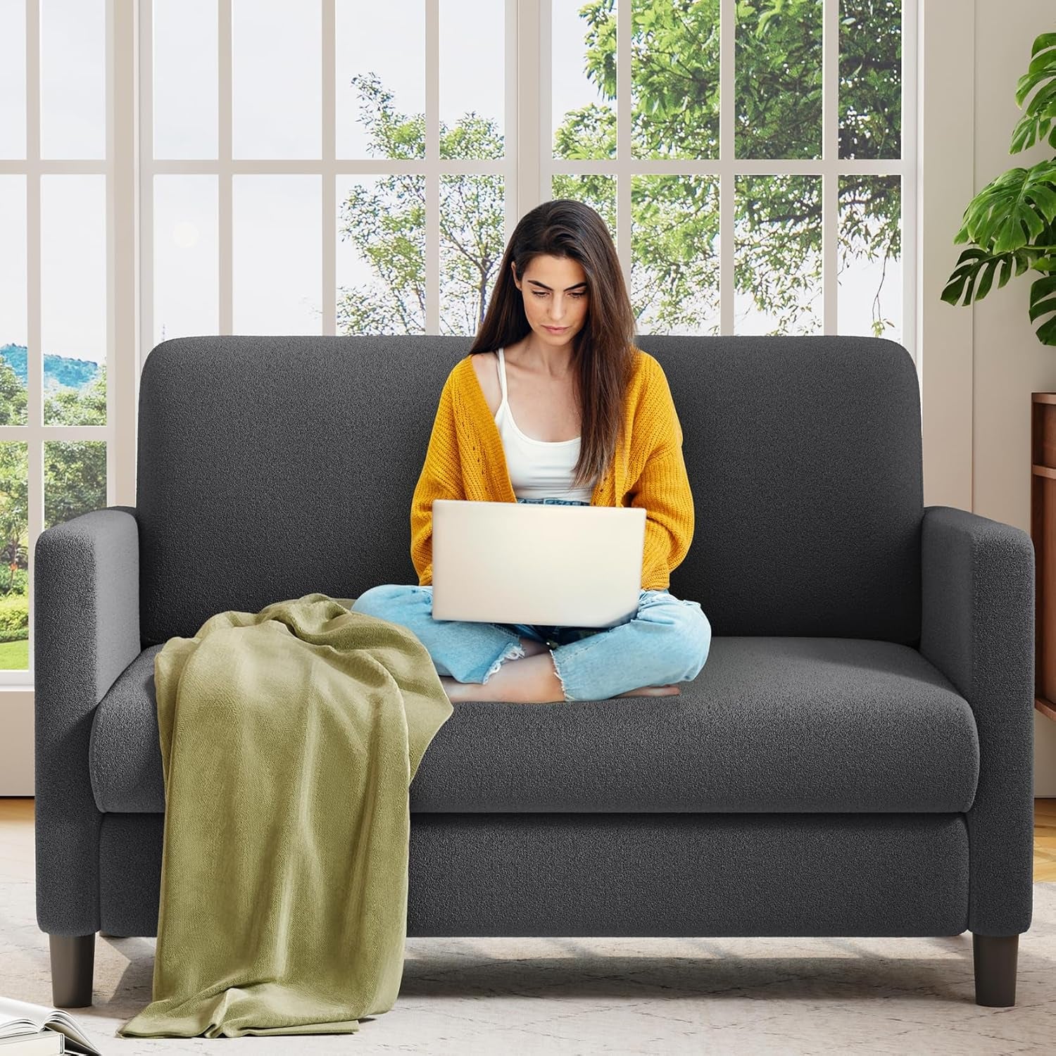 Dark-gray two-seat loveseat with a woman on a laptop and a blanket on the left