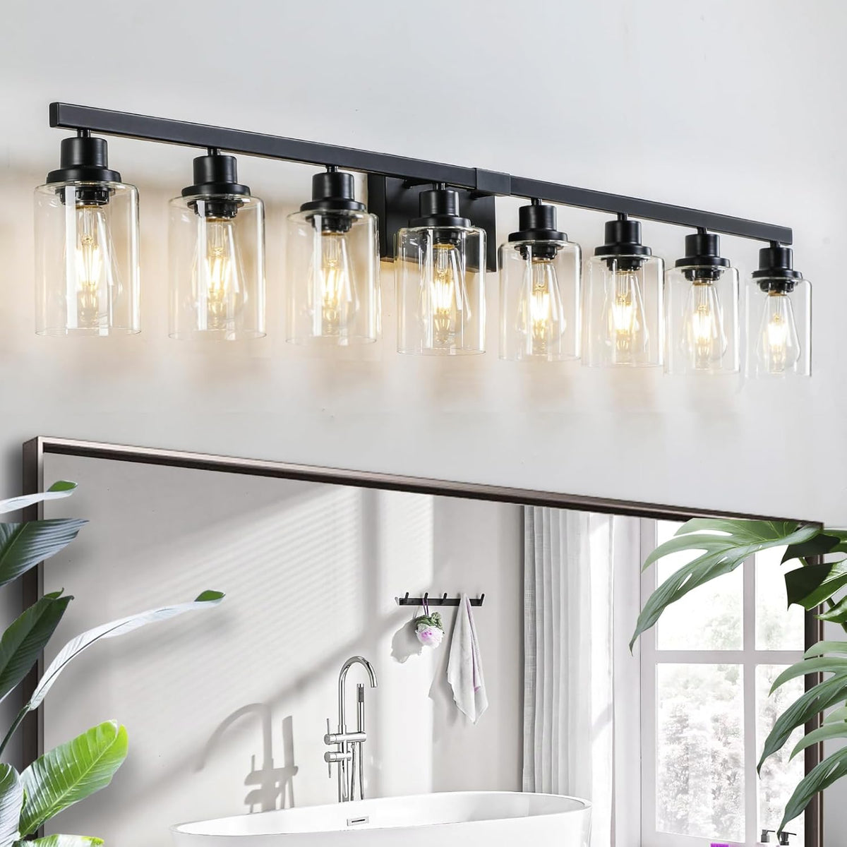 Wide view of an eight-light black vanity bar with clear glass shades mounted above a mirror and bathtub.
